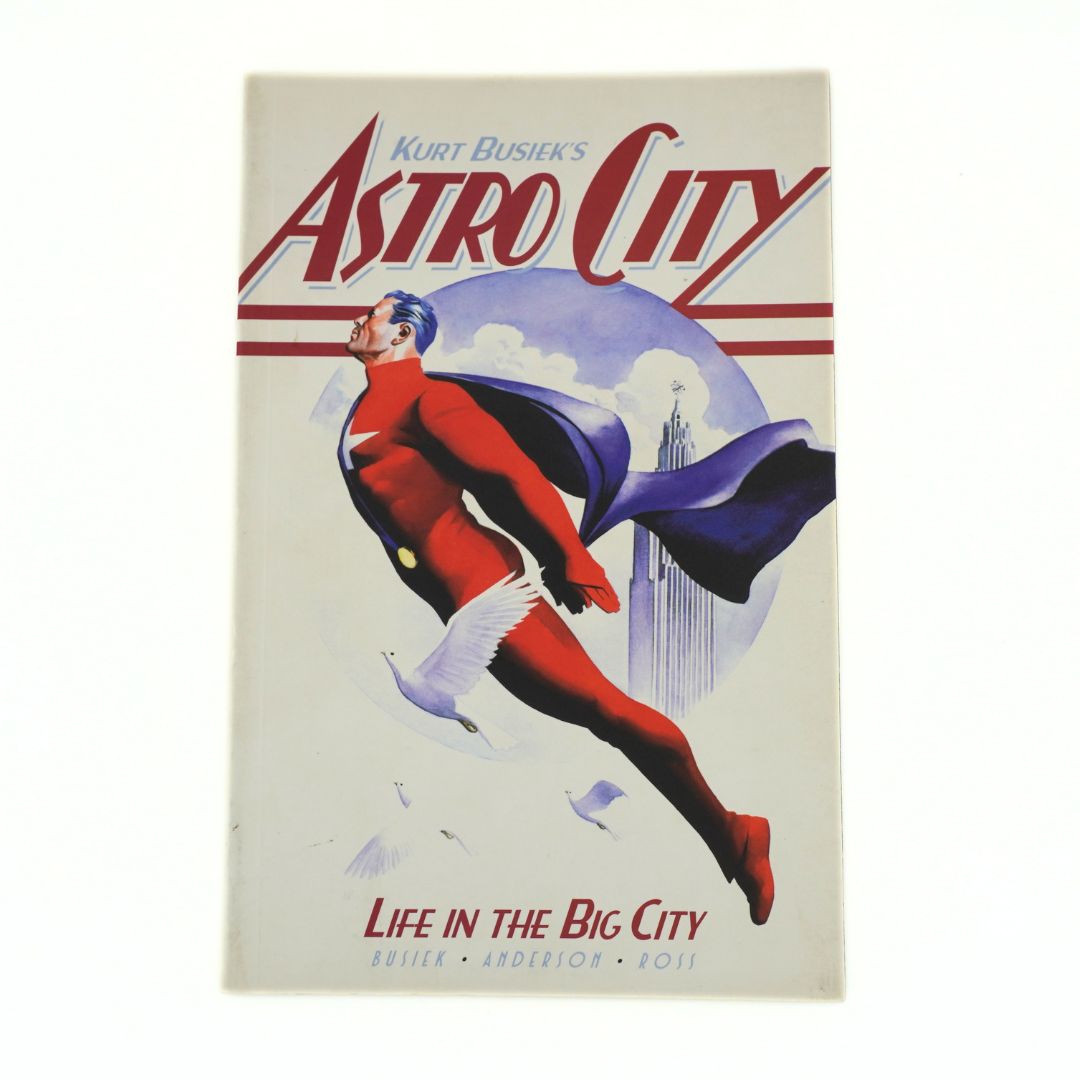 Vintage poster for Kurt Busiek's 'Astro City' featuring a retro superhero in a red suit and blue cape flying against a pale sky, with the title in large red letters and 'Life in the Big City' at the bottom.