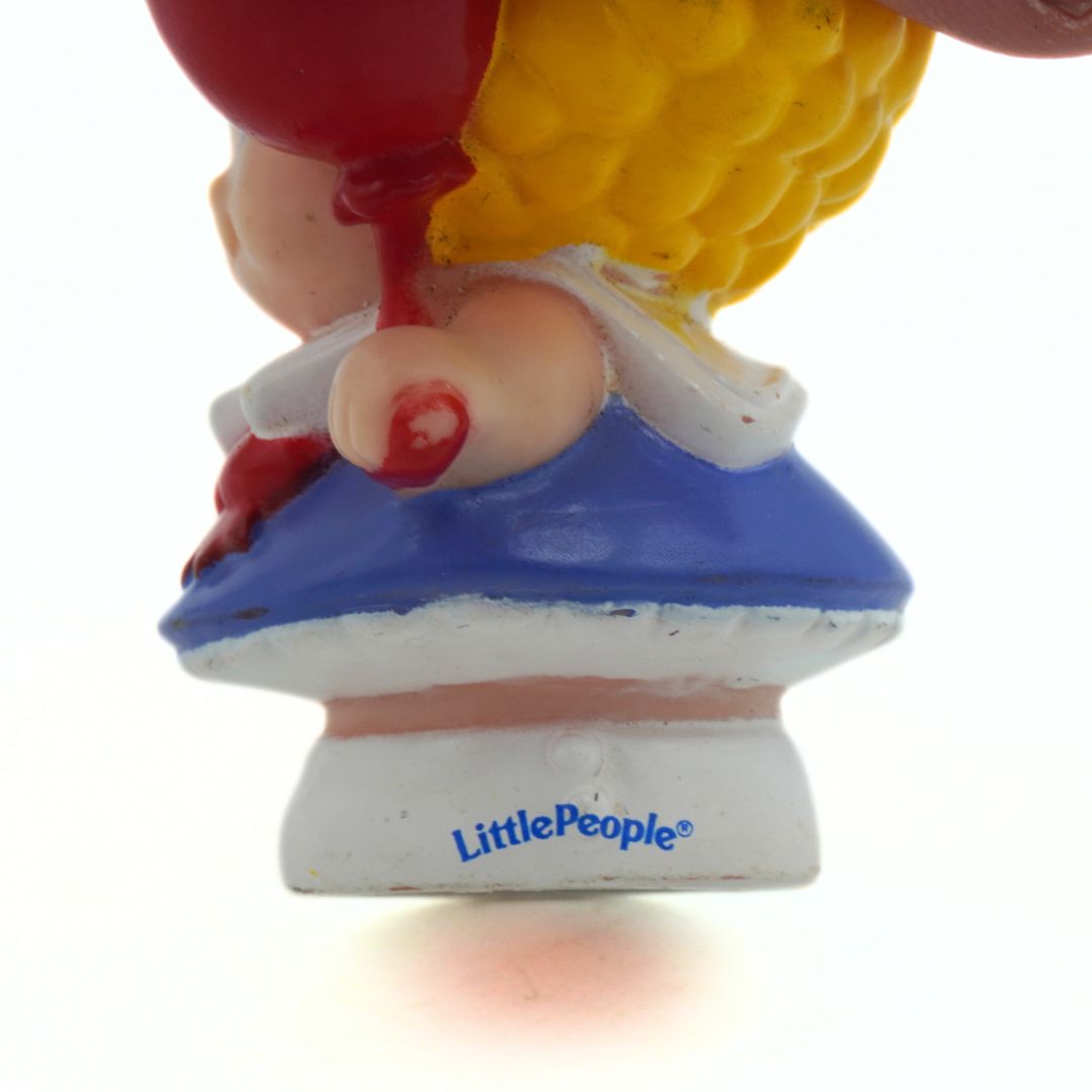 Toy figure with red hair, blue dress, and yellow shoes on a white background with 'Little People' branding.