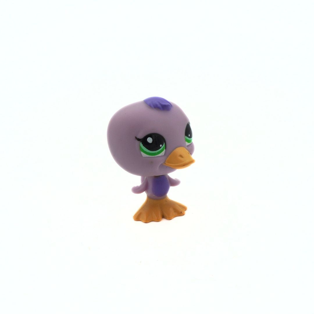 Small purple duck figurine with green eyes and orange feet on a white background