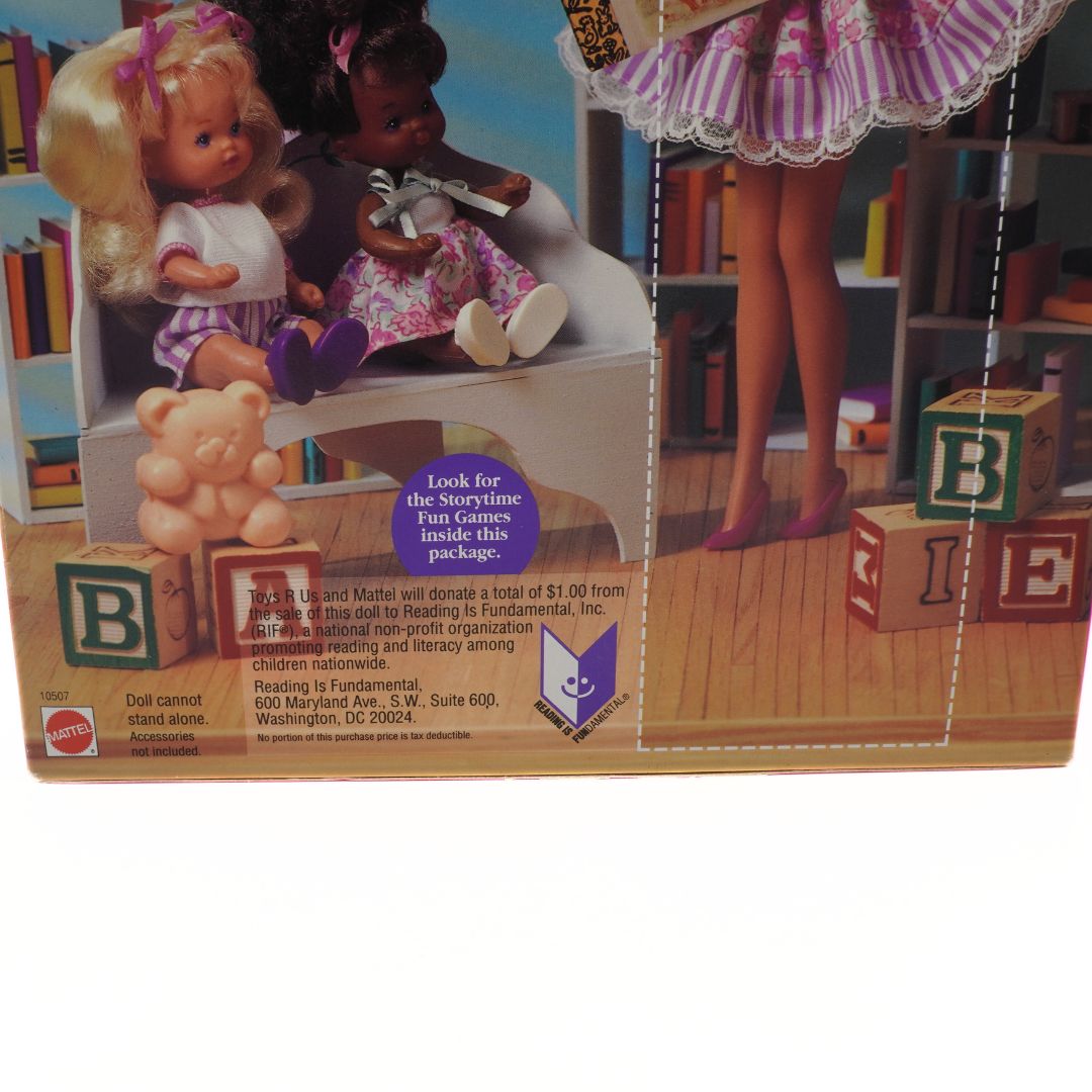 Toy packaging with dolls, blocks, and a teddy bear on a wooden floor.