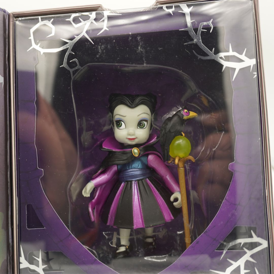 Toy figure of a witch in a purple outfit with a green topped staff, held in a decorative box.