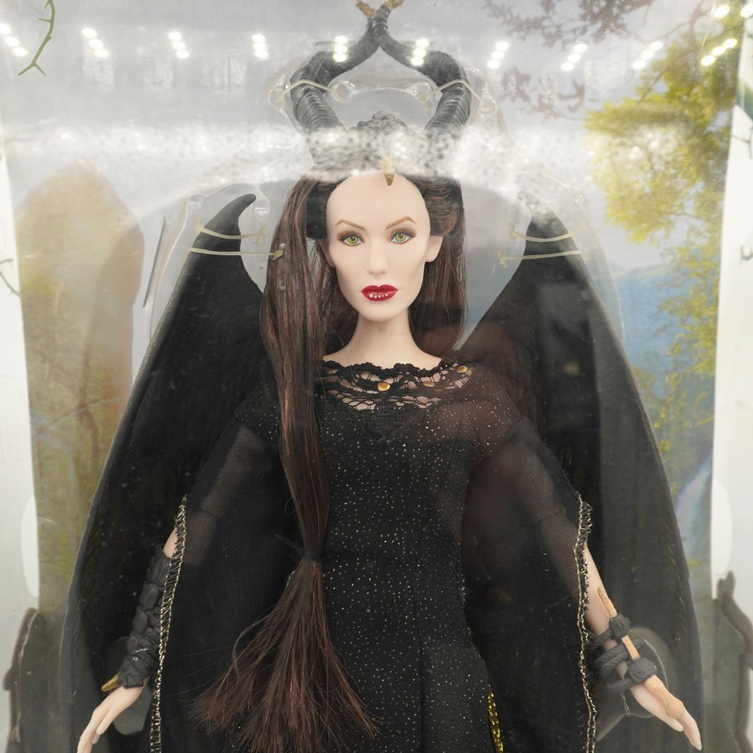 A Maleficent doll in a black gown and crown, displayed inside its clear plastic retail packaging.
