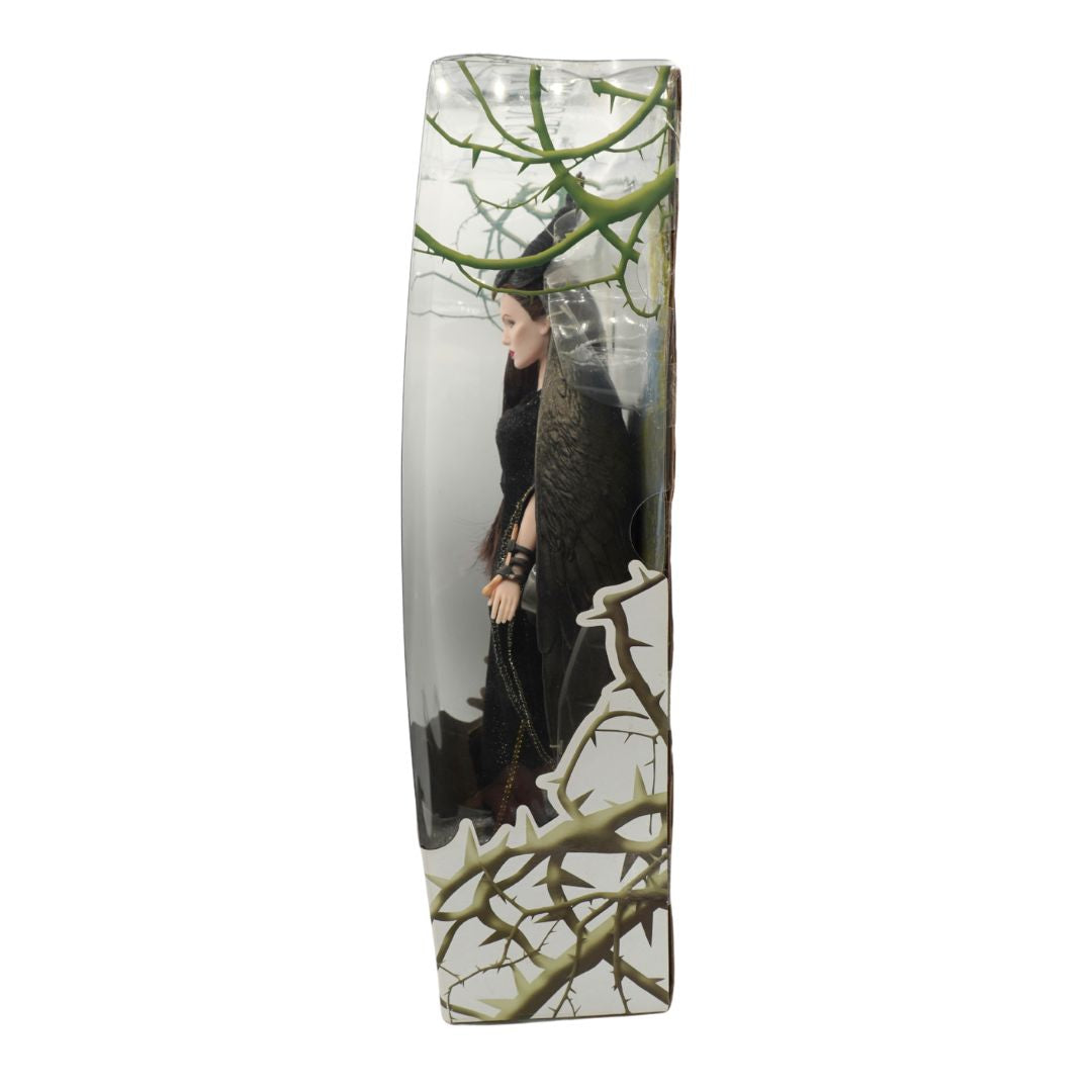 A tall, narrow rectangular plastic box featuring a doll in a black dress standing among bare thorny tree branches against a misty gray background.