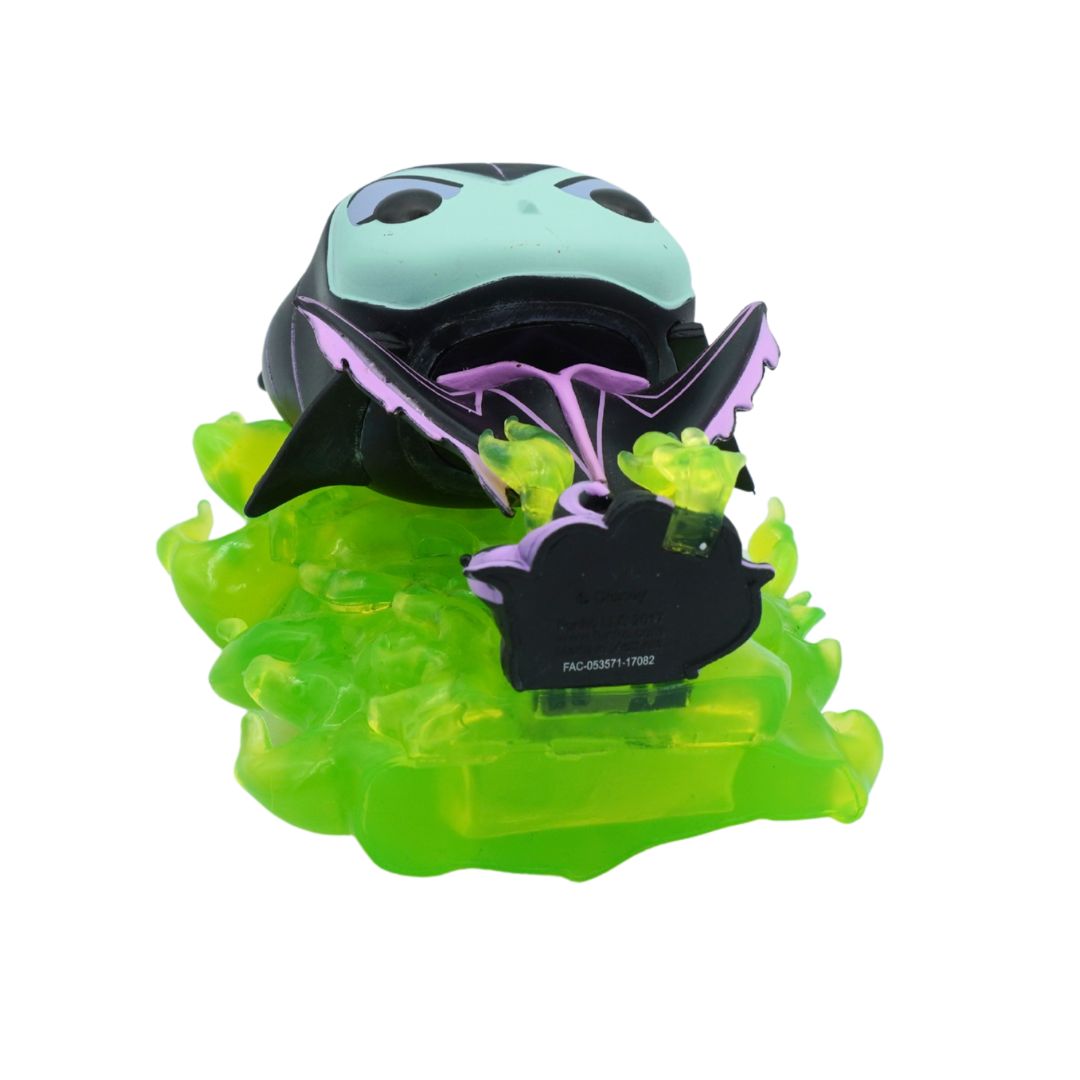 A small decorative figurine or toy featuring a pale mint-green and black face with purple bat-like wings, mounted on a translucent bright green base against a plain white background.