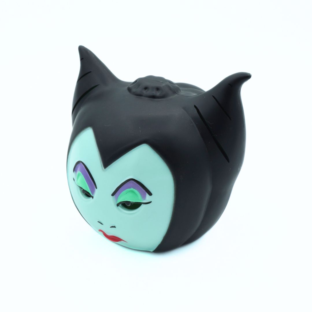 A Maleficent-themed squishy toy with a black cat-ear hat and a pale mint green face, featuring painted purple eyebrows, green eyes, and red lips, shown on a white background.