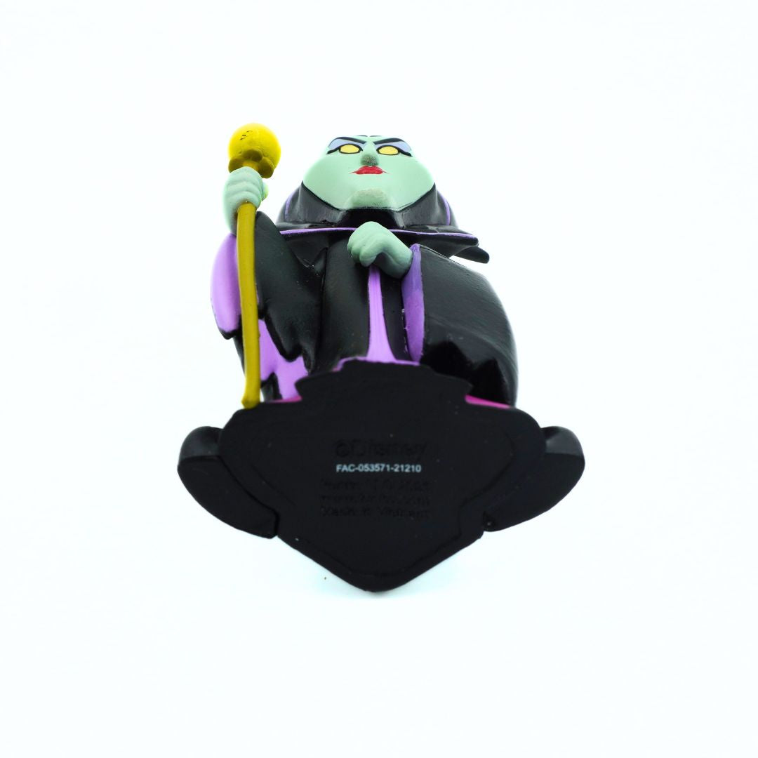 A collectible figurine of a green-skinned villain character in a black and purple robe, holding a yellow staff, seated on a black base against a white background.