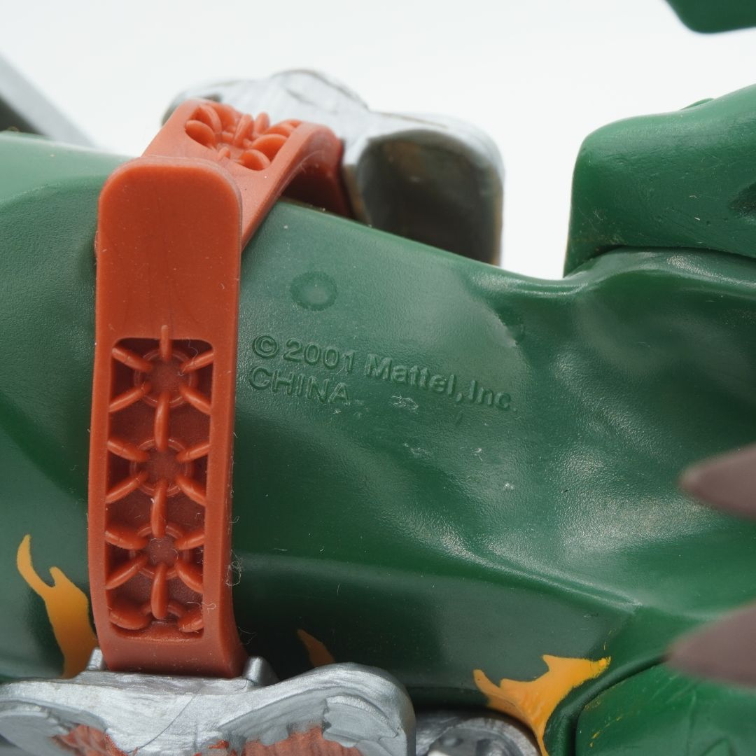 Close-up of a green toy figure with an orange strap, featuring Mattle, Inc. branding.