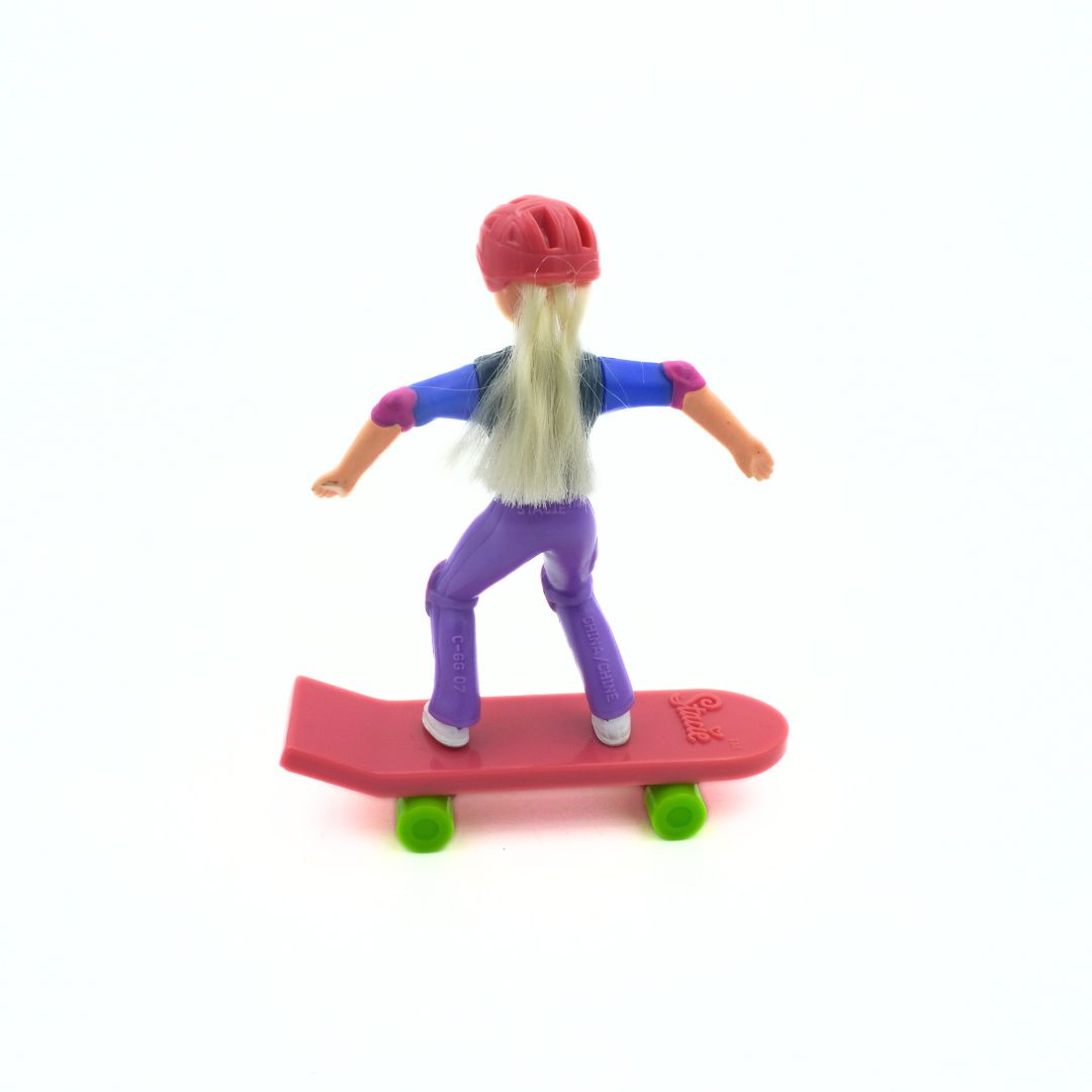 A Barbie Stacie doll wearing purple pants, a green and blue shirt, and a pink helmet riding a pink skateboard