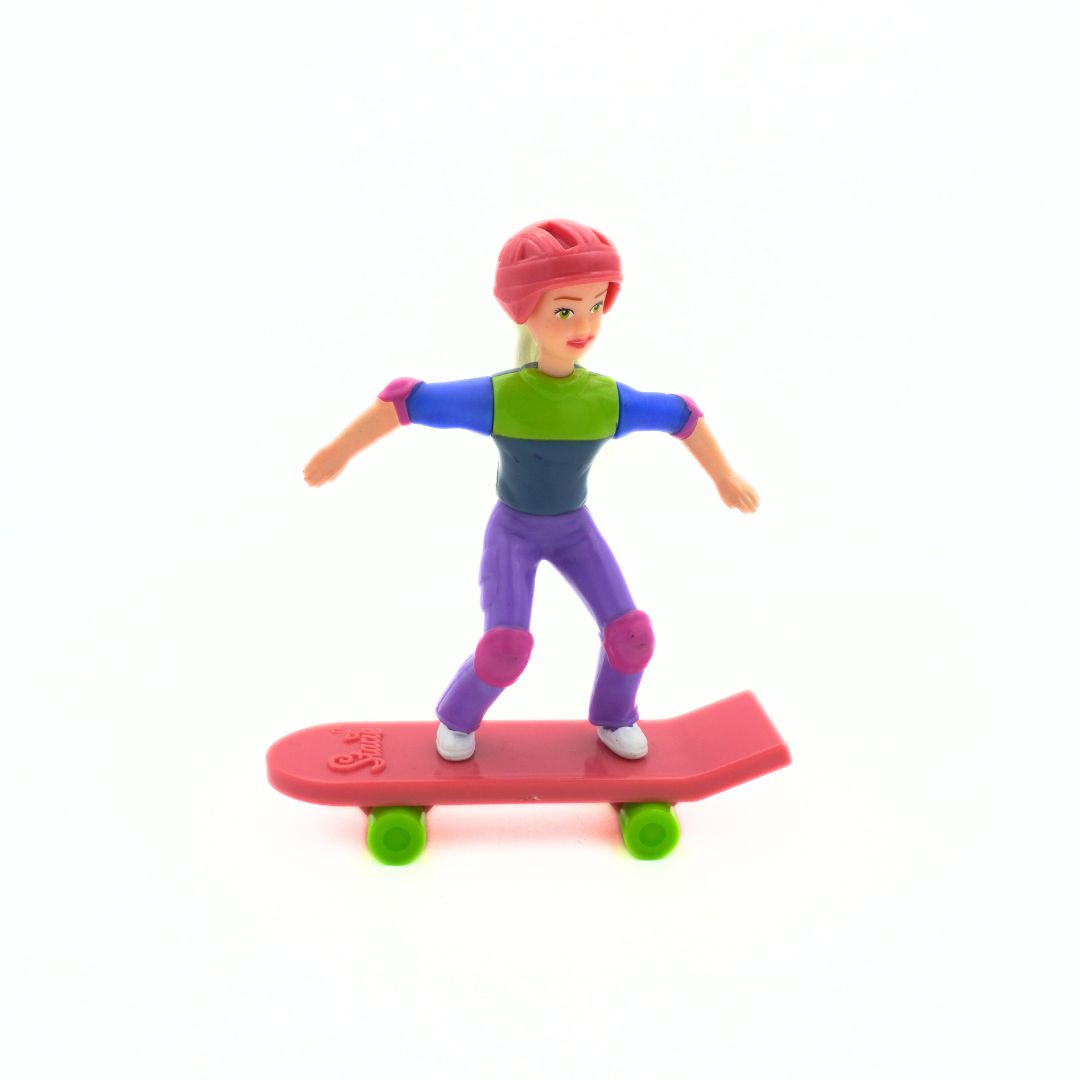 A Barbie Stacie doll wearing purple pants, a green and blue shirt, and a pink helmet riding a pink skateboard