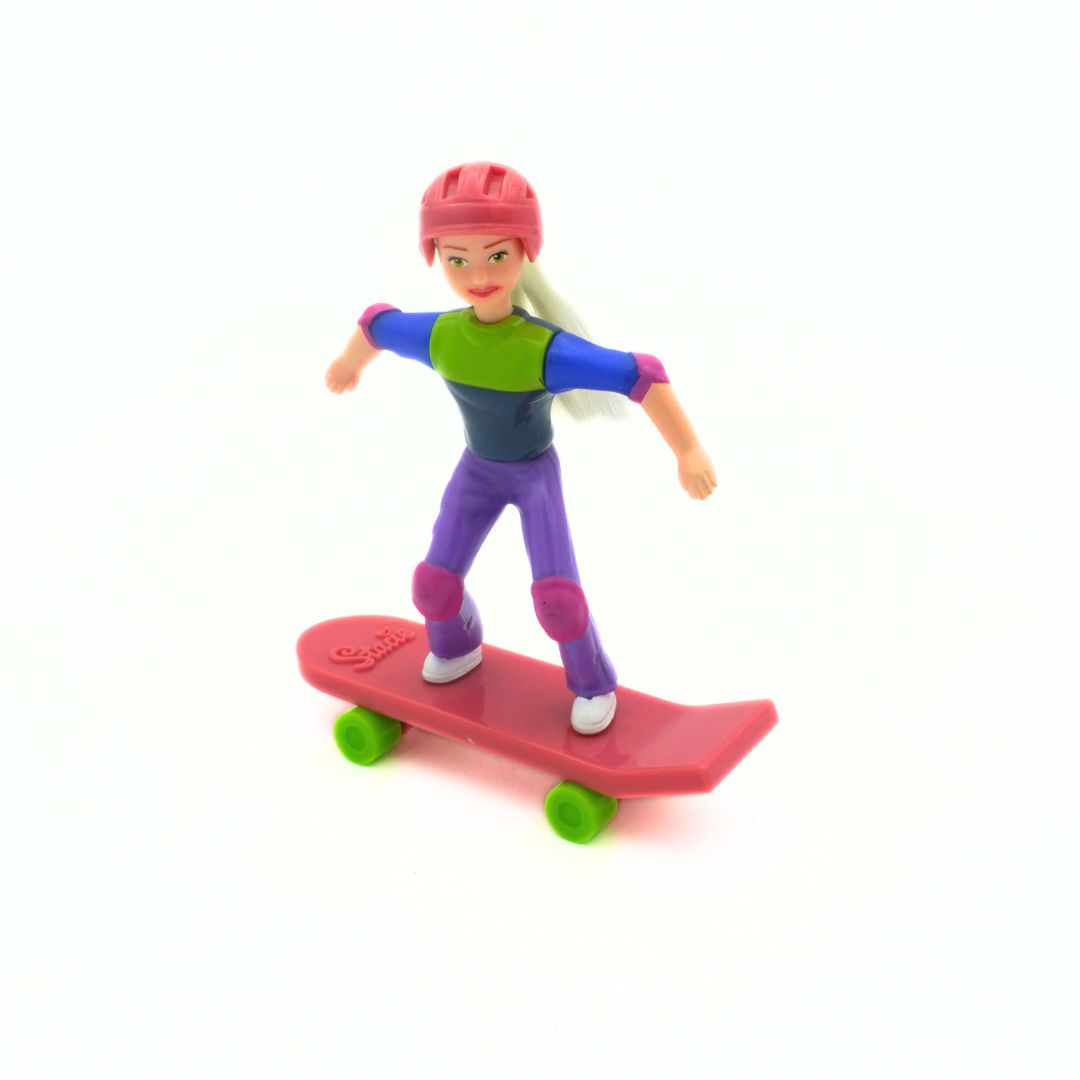 A Barbie Stacie doll wearing purple pants, a green and blue shirt, and a pink helmet riding a pink skateboard