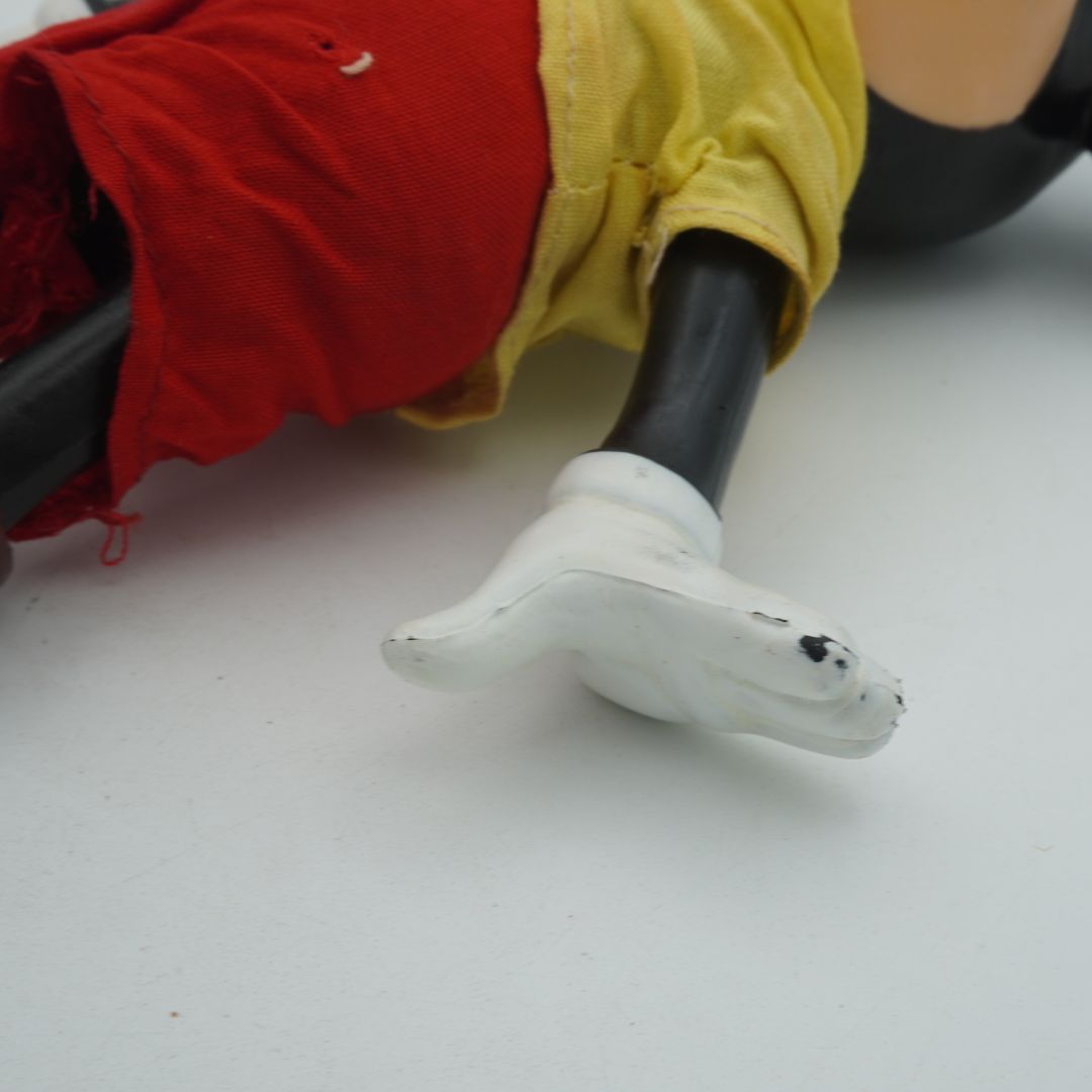 Close-up of a toy figure's leg with red pants, yellow shirt, and white shoes on a white background