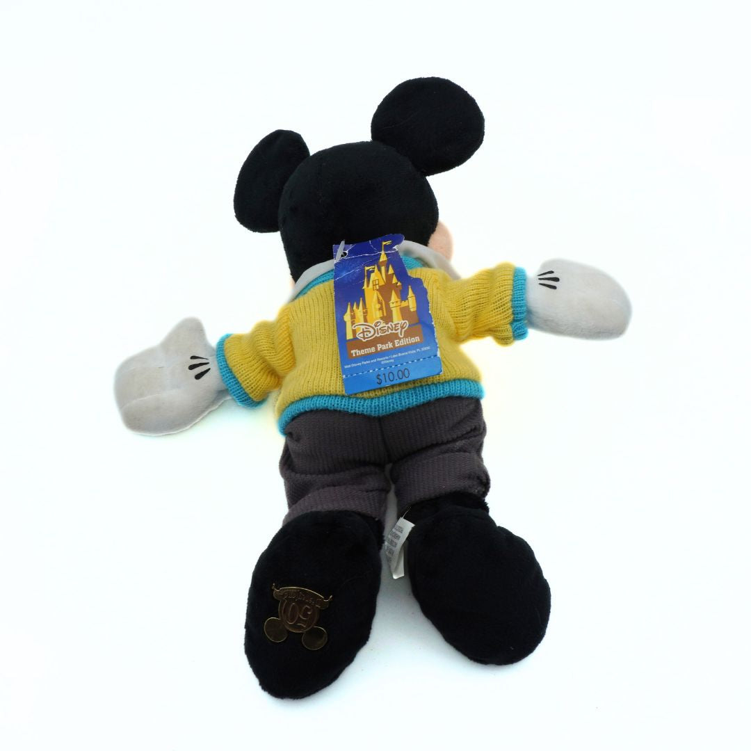Plush Mickey Mouse toy in a yellow sweater with a castle design on a white background