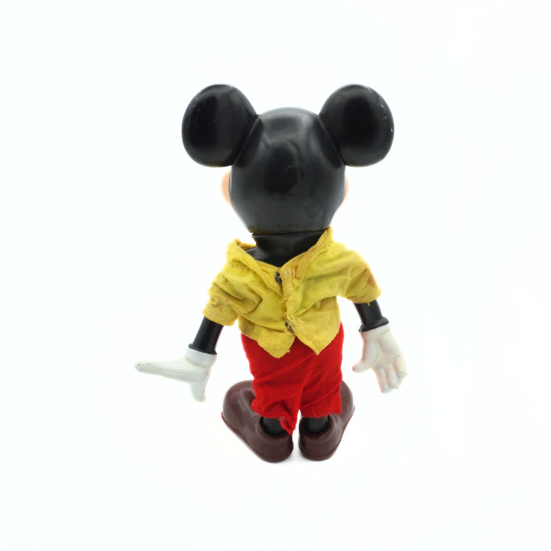 Toy figure of a character with black hair, yellow shirt, and red pants on a white background