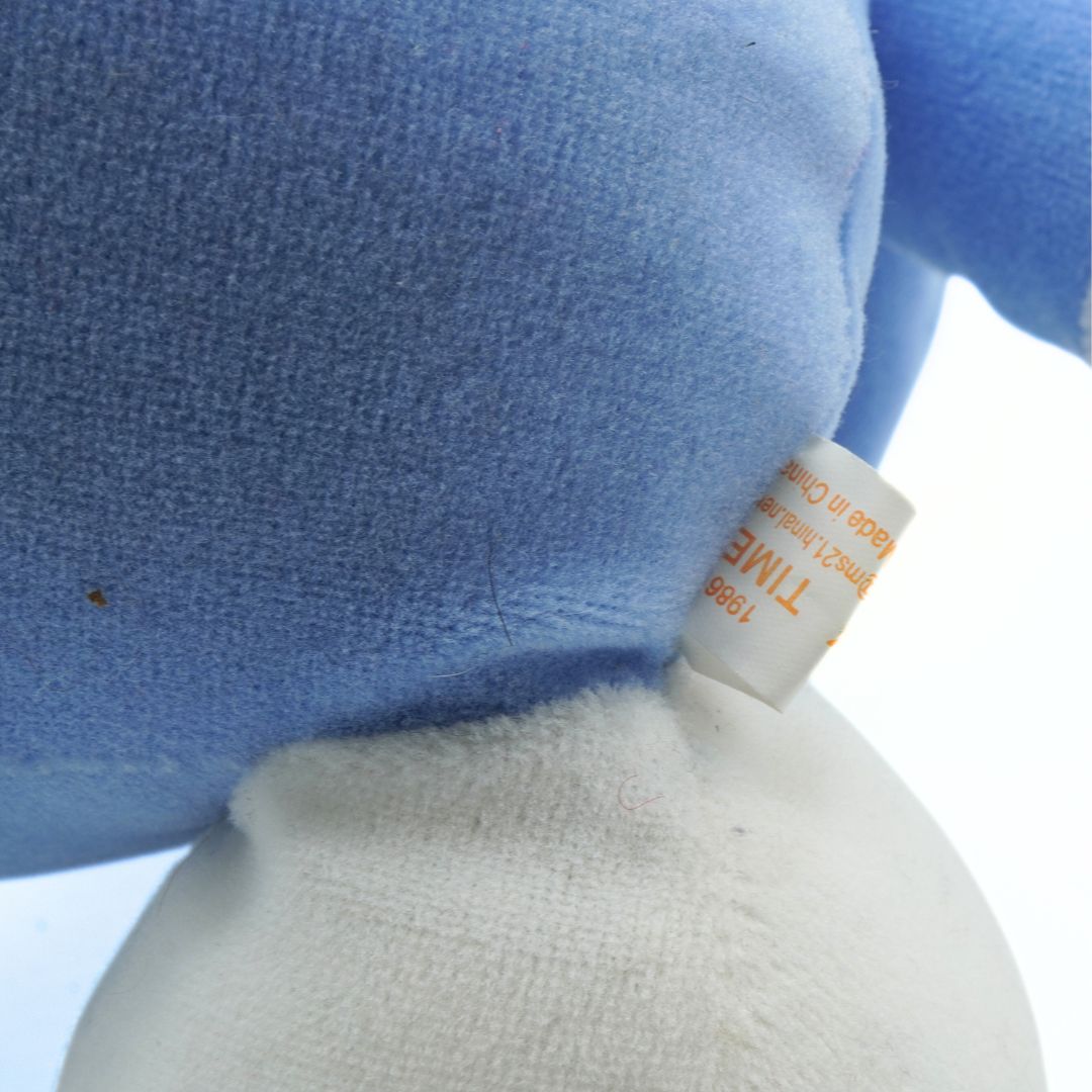 Close-up of a blue plush toy with a white tag on a light background