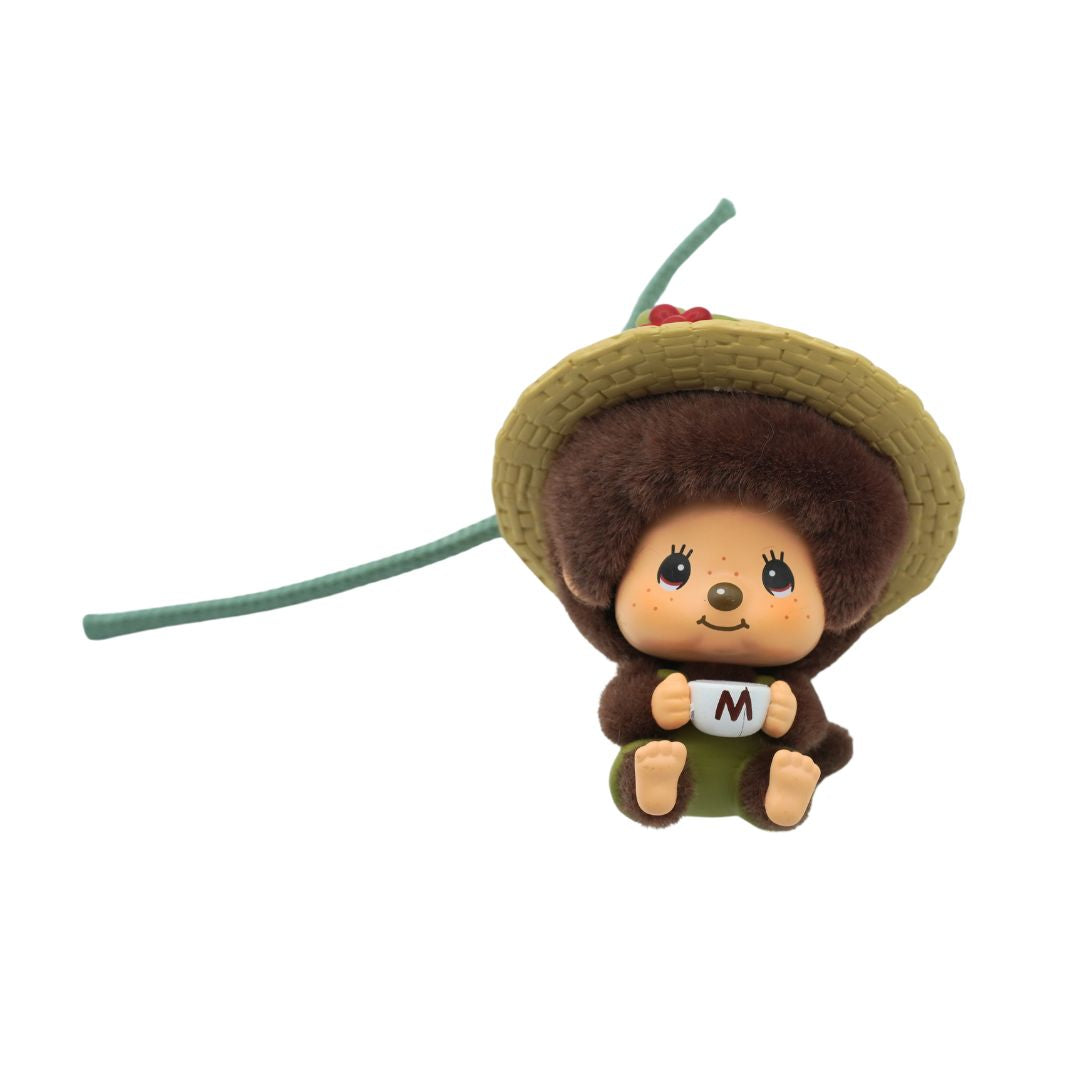 A small brown Monchhichi figurine wearing a brown hat and holding a white mug