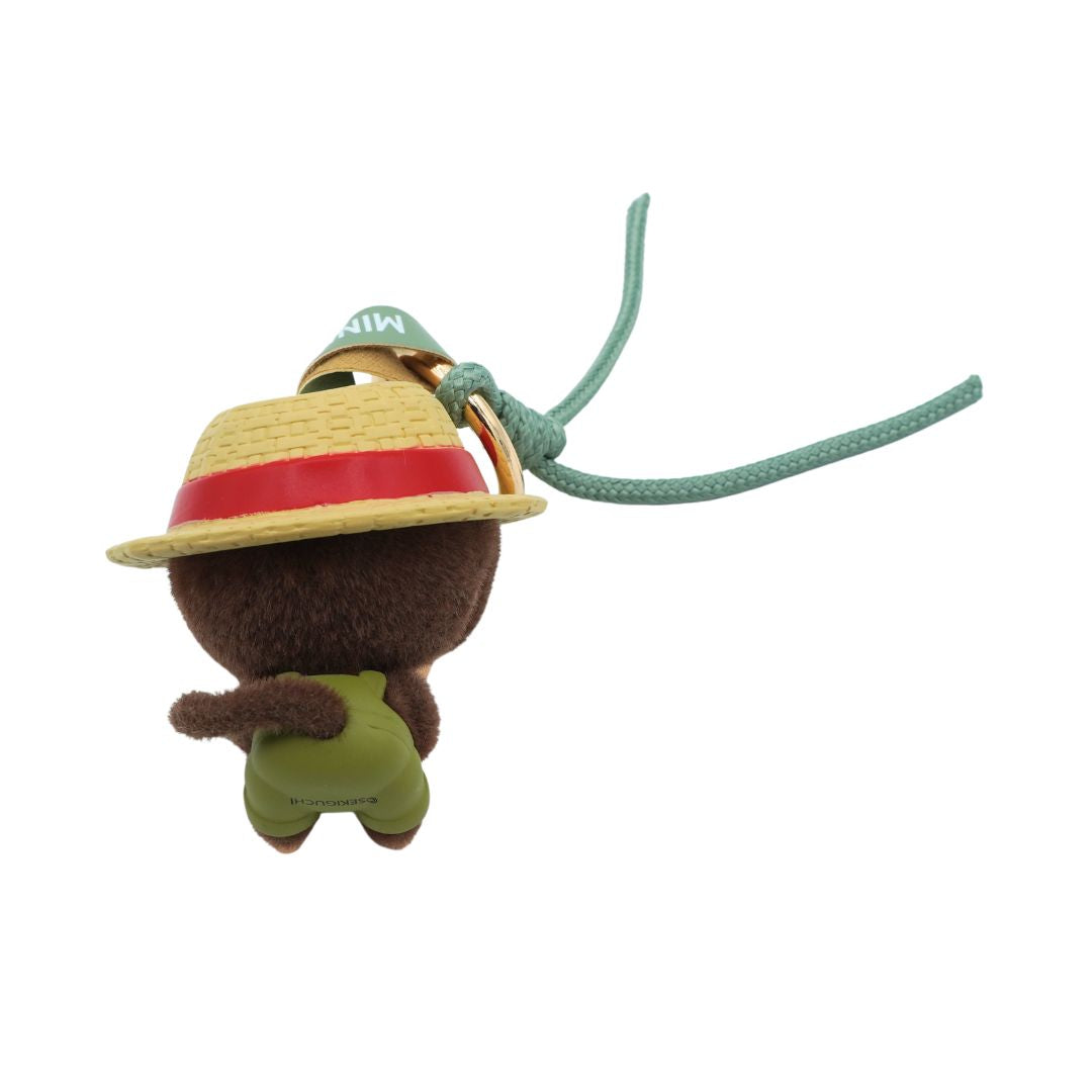 A small brown Monchhichi figurine wearing a brown hat and green overalls.