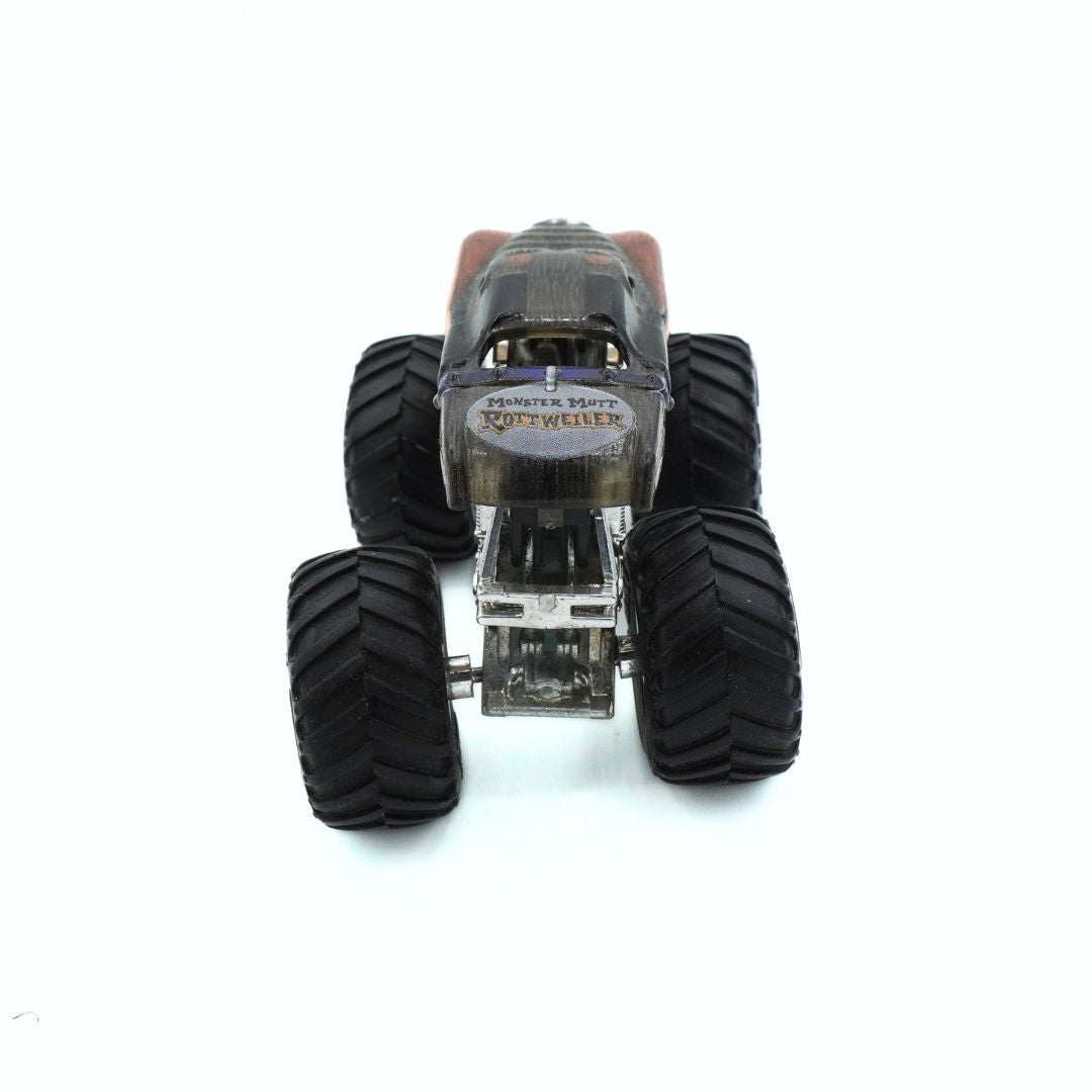 A small monster truck toy with large black off-road tires, a clear plastic hood, and a silver chassis, photographed from the rear on a white background.