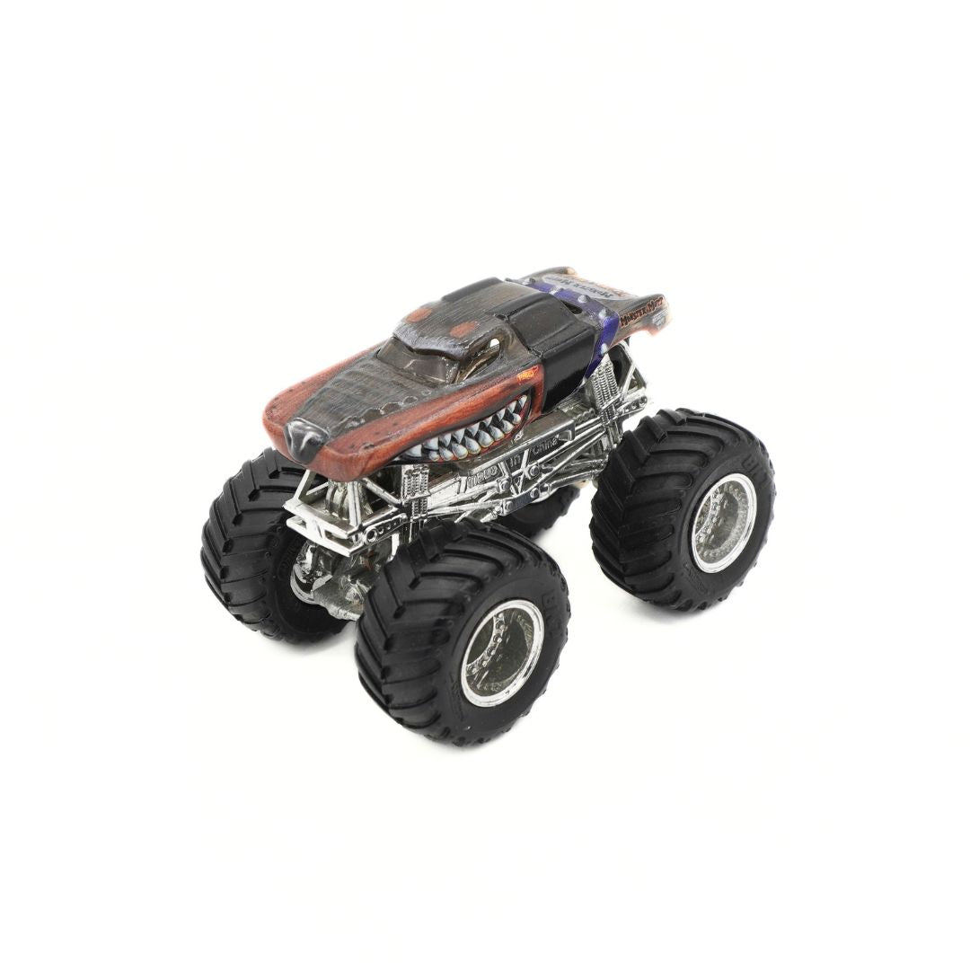 A miniature diecast model of a monster truck with oversized black tires, a detailed silver chassis, and a body featuring a red hood and a dark gray roof, shown on a plain white background.