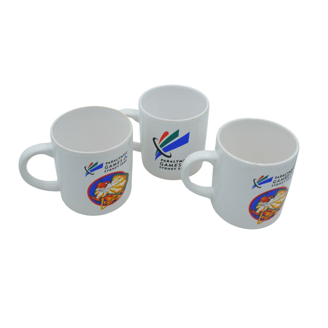 Three white mugs with Paralympic Games Sydney 2000 logos on a white background