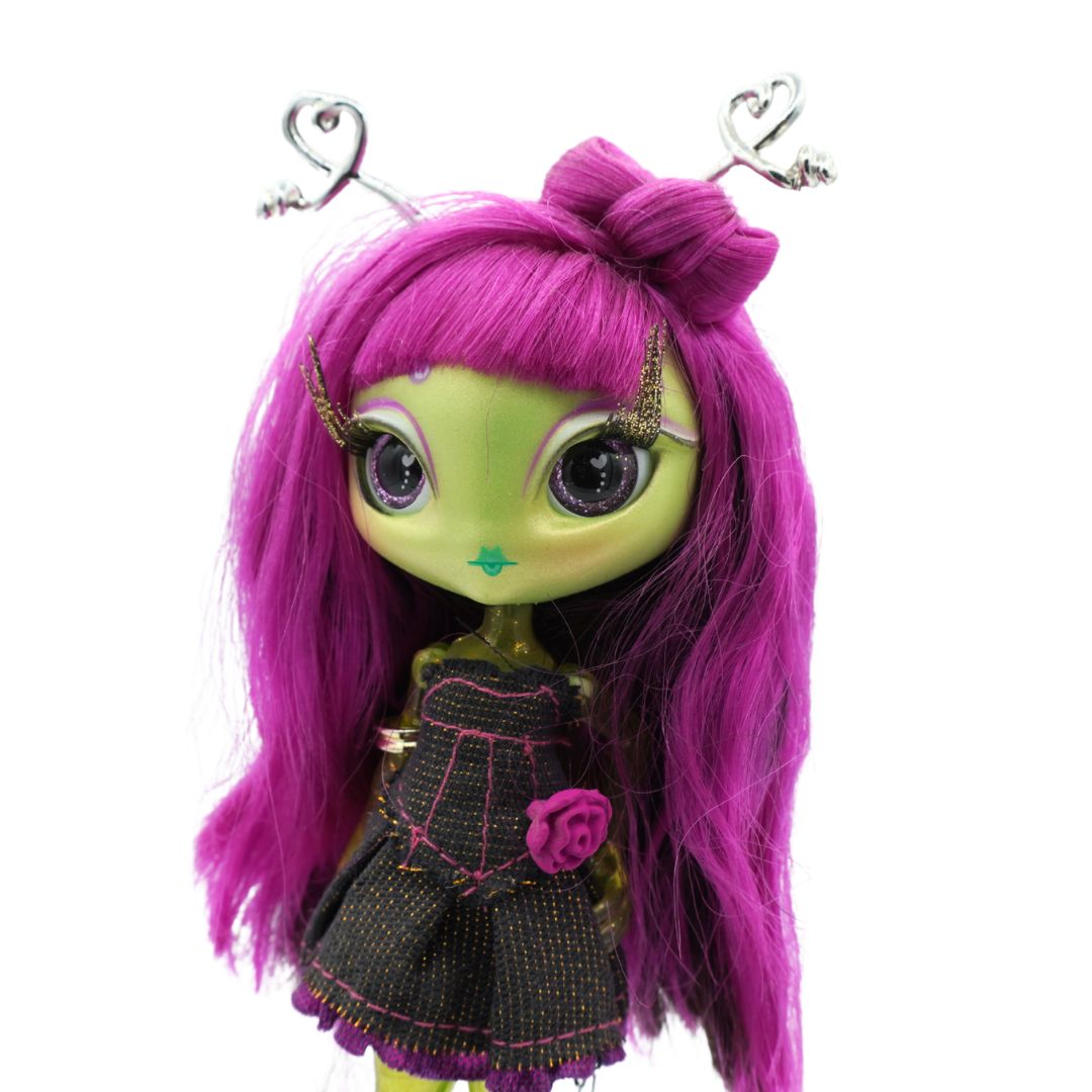 A Novi Star doll with green legs and purple hair, wearing a dark denim dress and standing on a cream coloured stand