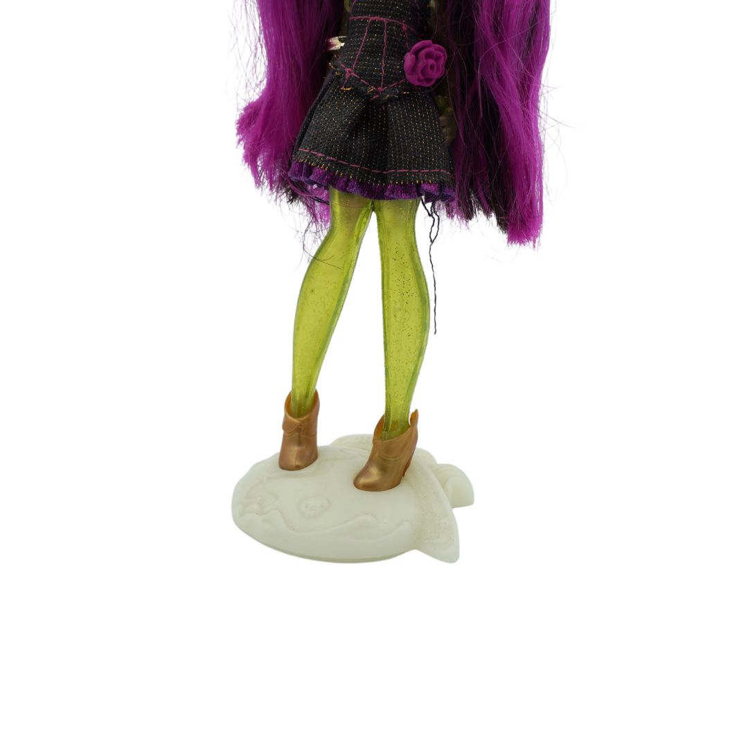 A Novi Star doll with green legs and purple hair, wearing a dark denim dress and standing on a cream coloured stand