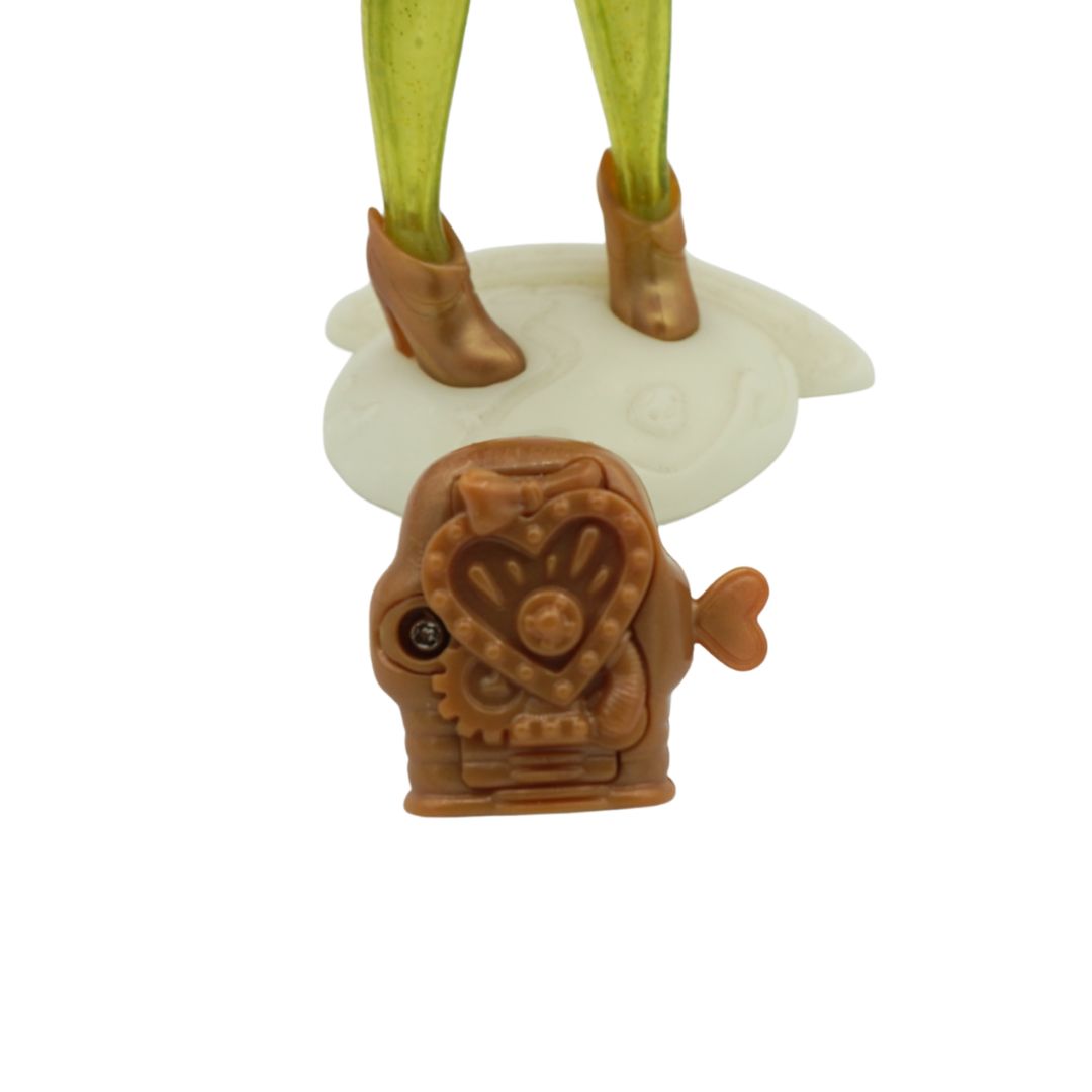 A Novi Star doll with green legs and purple hair, wearing a dark denim dress and standing on a cream coloured stand with a brown backpack