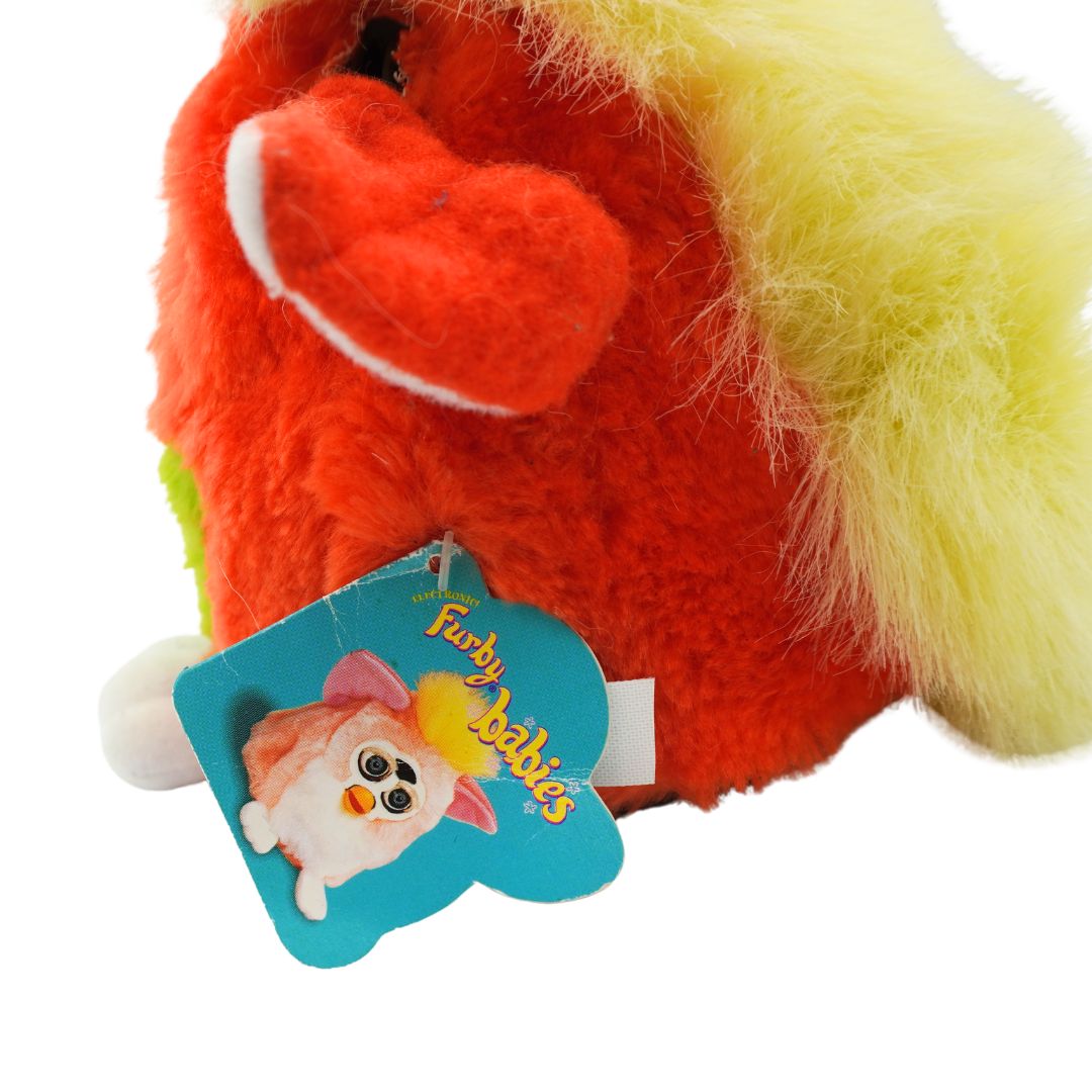 An orange and green Furby with yellow hair and blue eyes, photographed against a white background