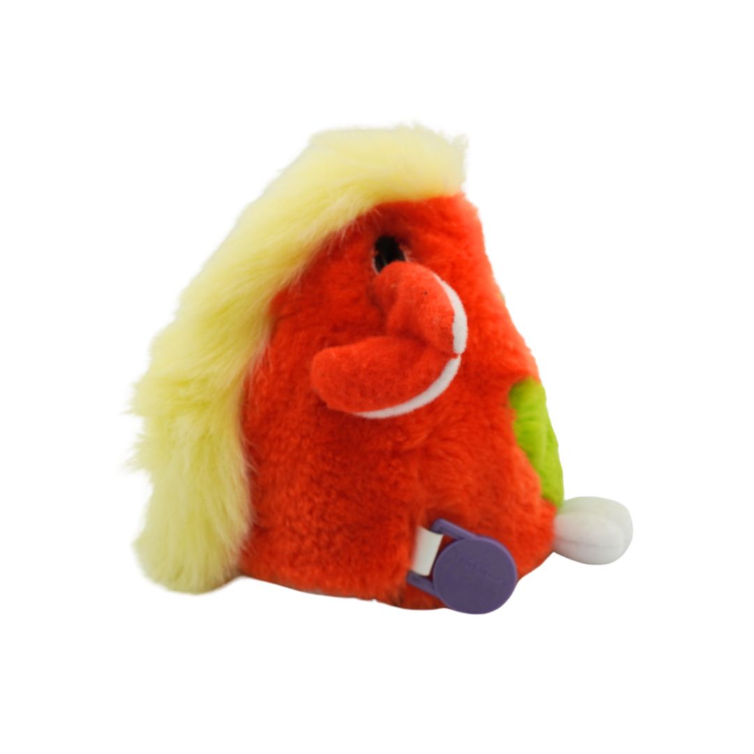 An orange and green Furby with yellow hair and blue eyes, photographed against a white background