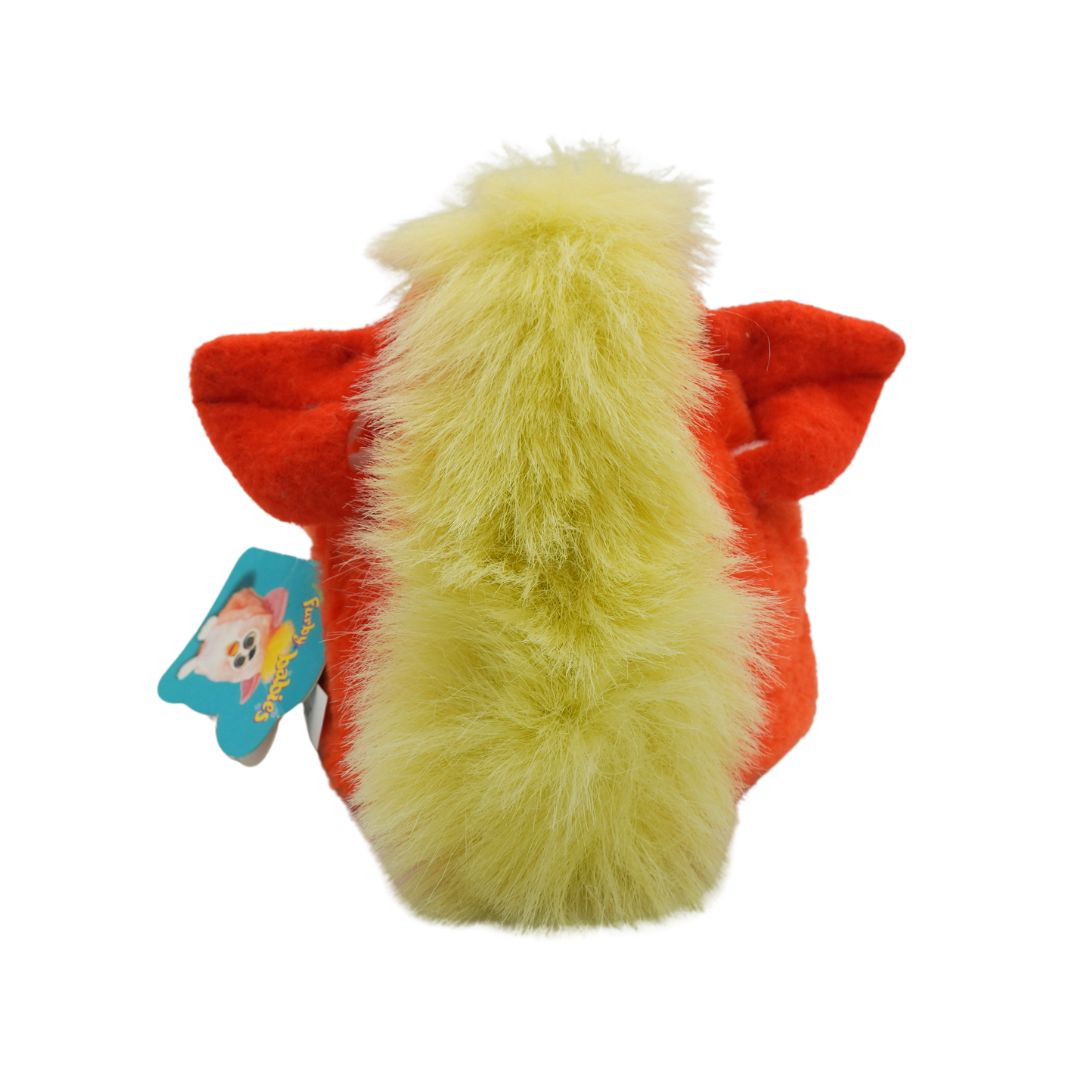 An orange and green Furby with yellow hair and blue eyes, photographed against a white background
