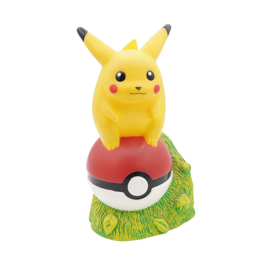 Pikachu figurine on a grassy base with a Poké Ball underneath on a white background