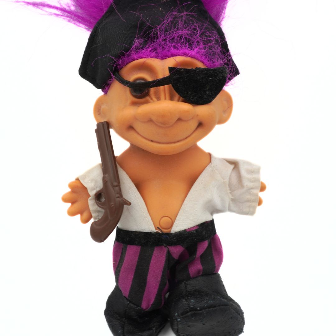 Pirate-themed toy figure with purple hair, eye patch and toy gun on a white background