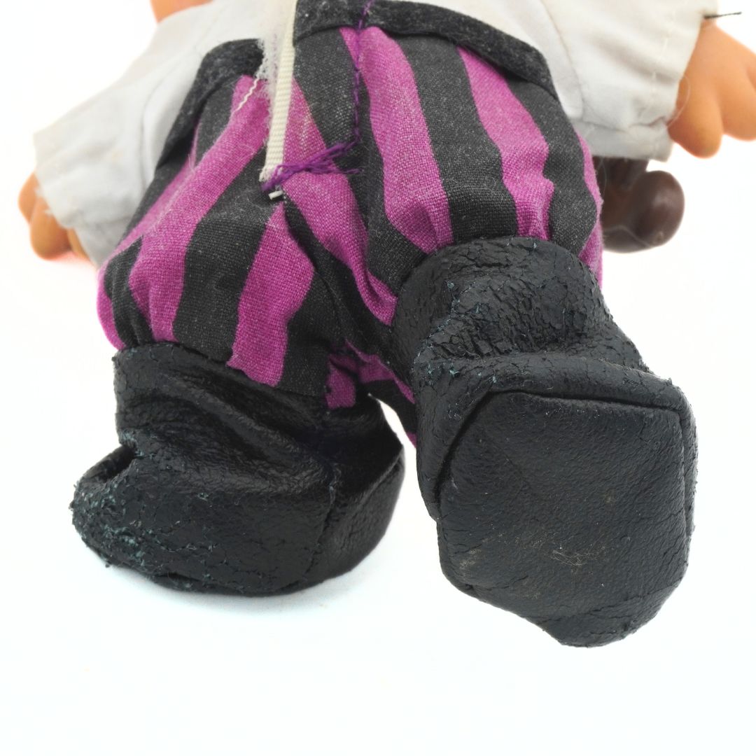 Close-up of a toy figure's feet wearing black and purple striped shoes on a white background