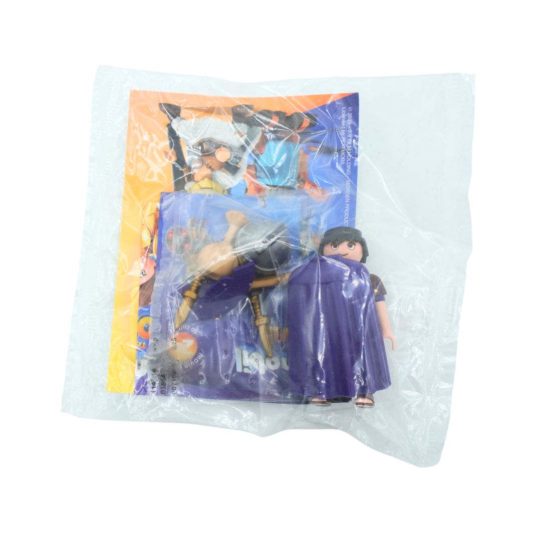A toy action figure of a character in a purple cloak standing next to its printed backing card, sealed inside a clear plastic bag on a white background.