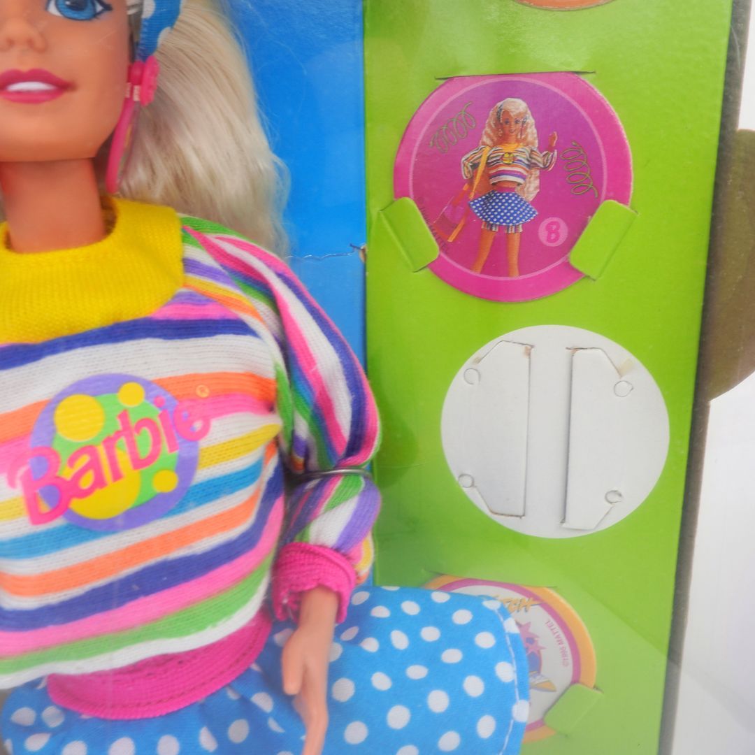 Barbie doll wearing a colorful striped shirt with 'Barbie' logo next to its packaging.