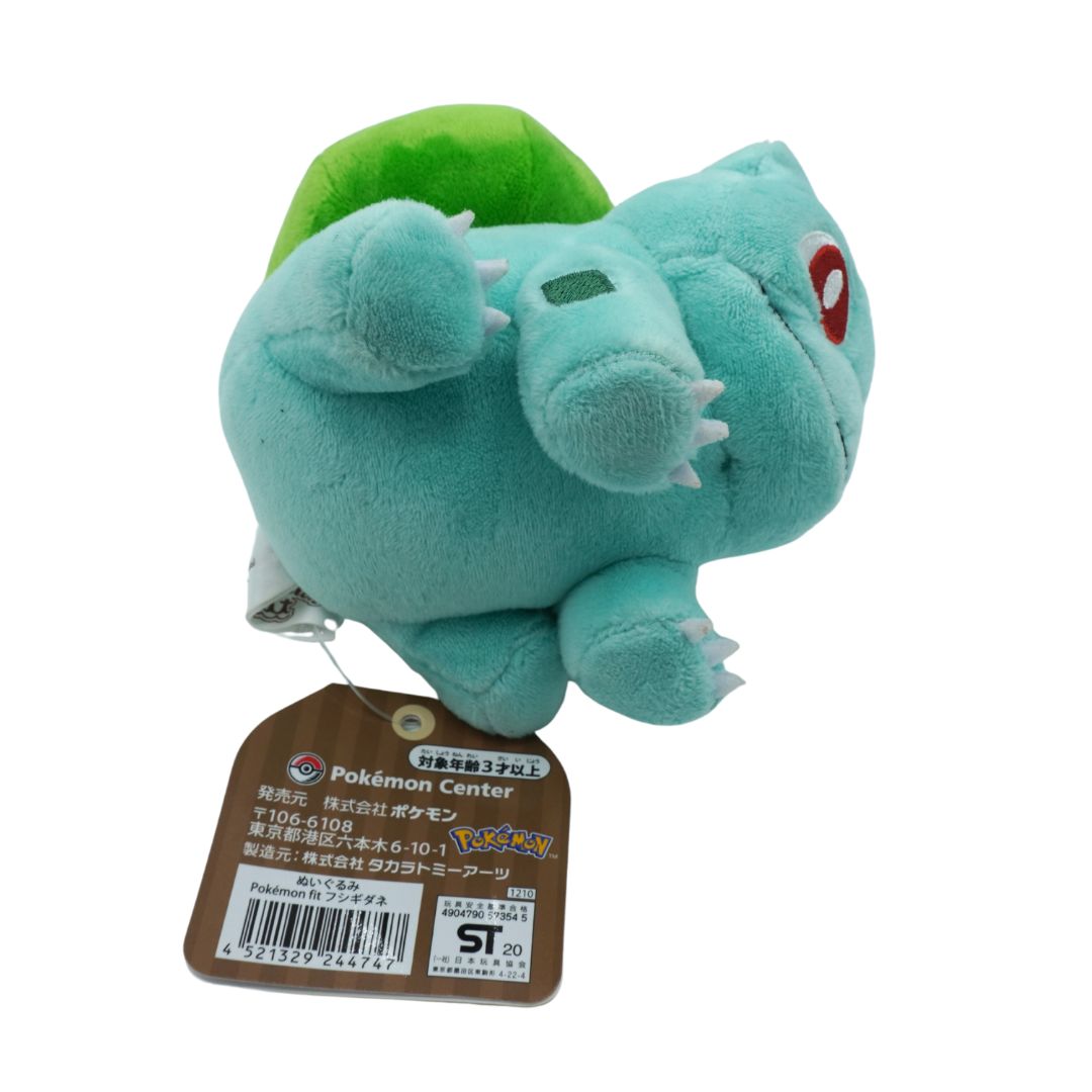 Plush toy of a turquoise creature with a green shell, attached to a tag, on a white background.