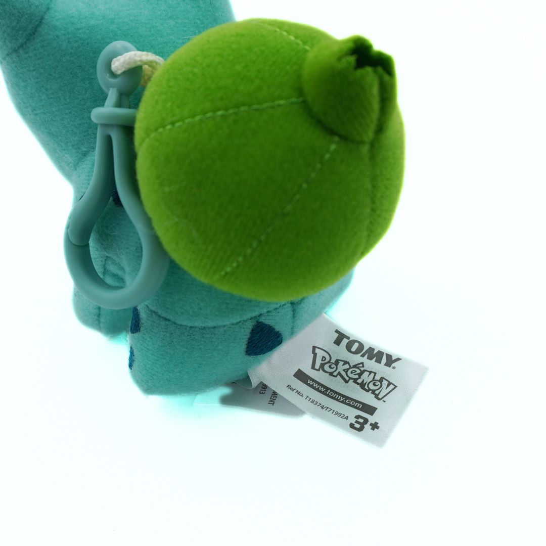 Green plush toy with a clip on a white background, featuring a Tomy tag.