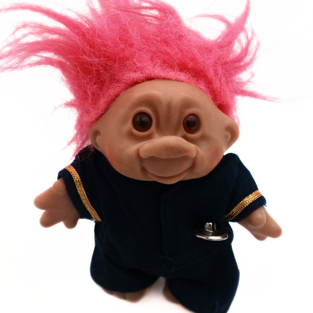 Photo of a pink haired Troll doll in a blue and gold uniform with a silver button