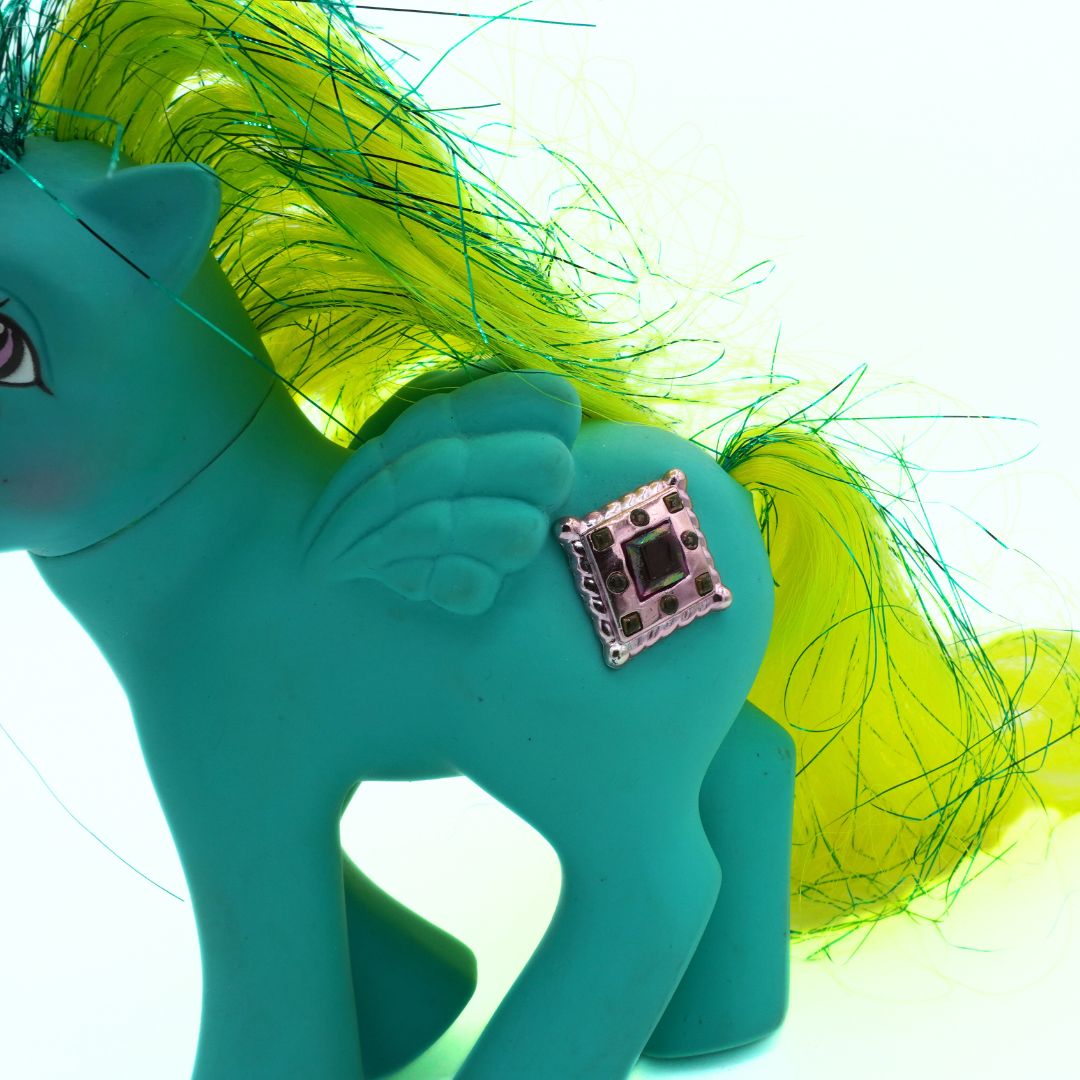 Close-up of a teal pony figurine with a yellow mane on a white background