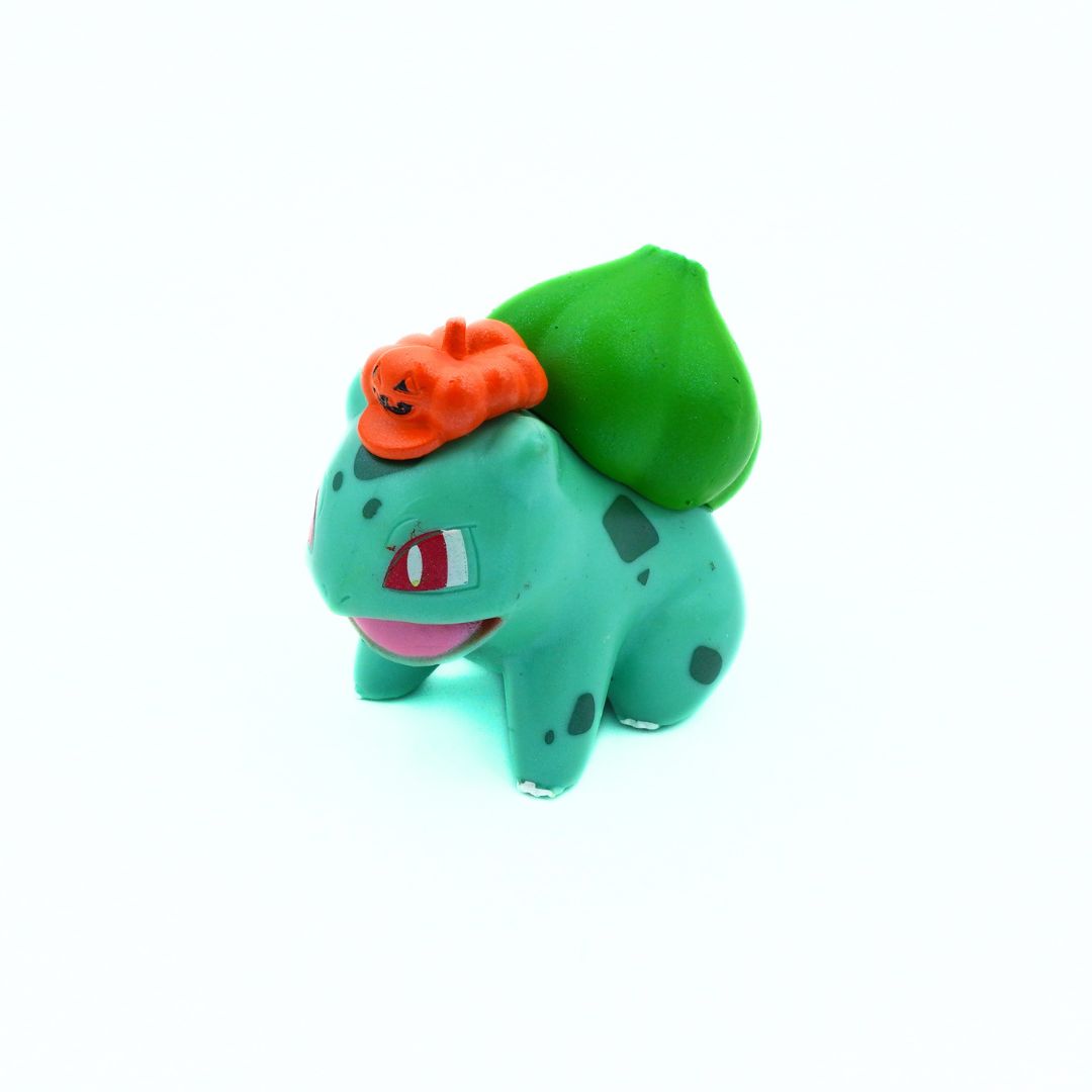 Toy figure of a green dinosaur-like creature with an orange hat on a white background