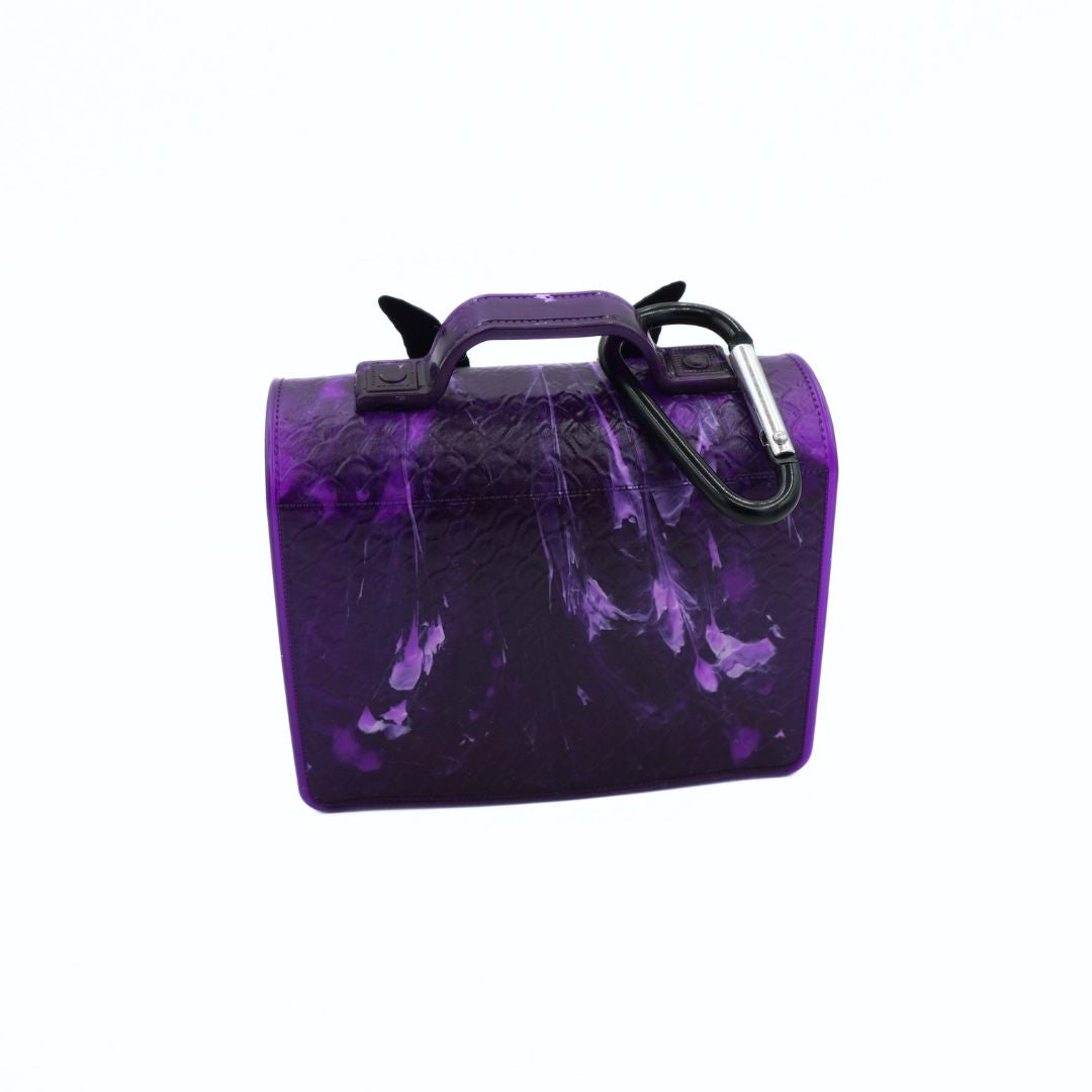A small structured handbag in glossy purple textured leather with a black carabiner attached to the side and a top handle, shown on a plain white background.