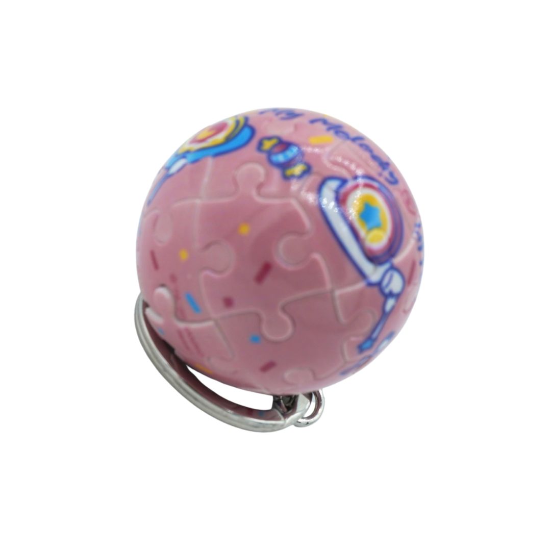 A pink spherical keychain charm featuring a jigsaw puzzle pattern with colorful cartoon astronaut graphics, attached to a silver metal ring, shown on a plain white background.