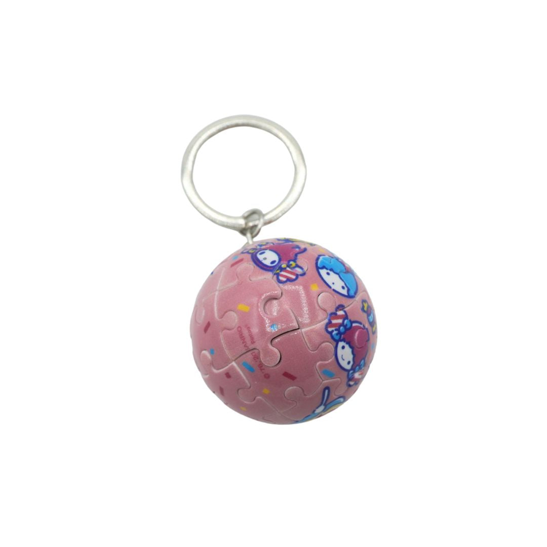 A pink spherical jigsaw puzzle charm featuring cartoon characters, attached to a silver metal key ring, shown against a plain white background.
