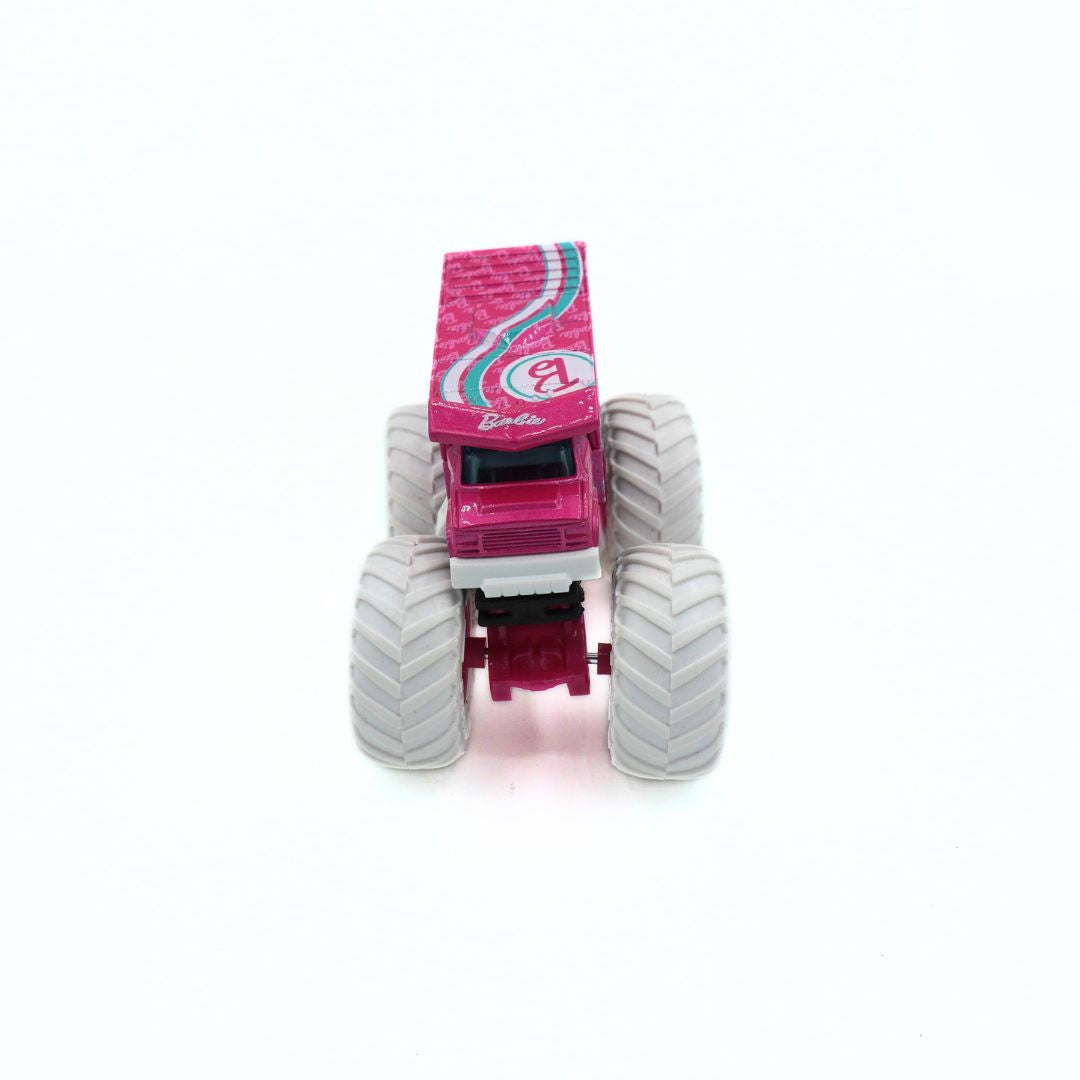 A pink and white Barbie monster truck toy with large gray treaded tires, shown from a front-facing perspective on a white background.