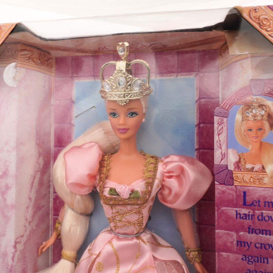 Barbie doll in a pink dress with a crown in a packaging box.