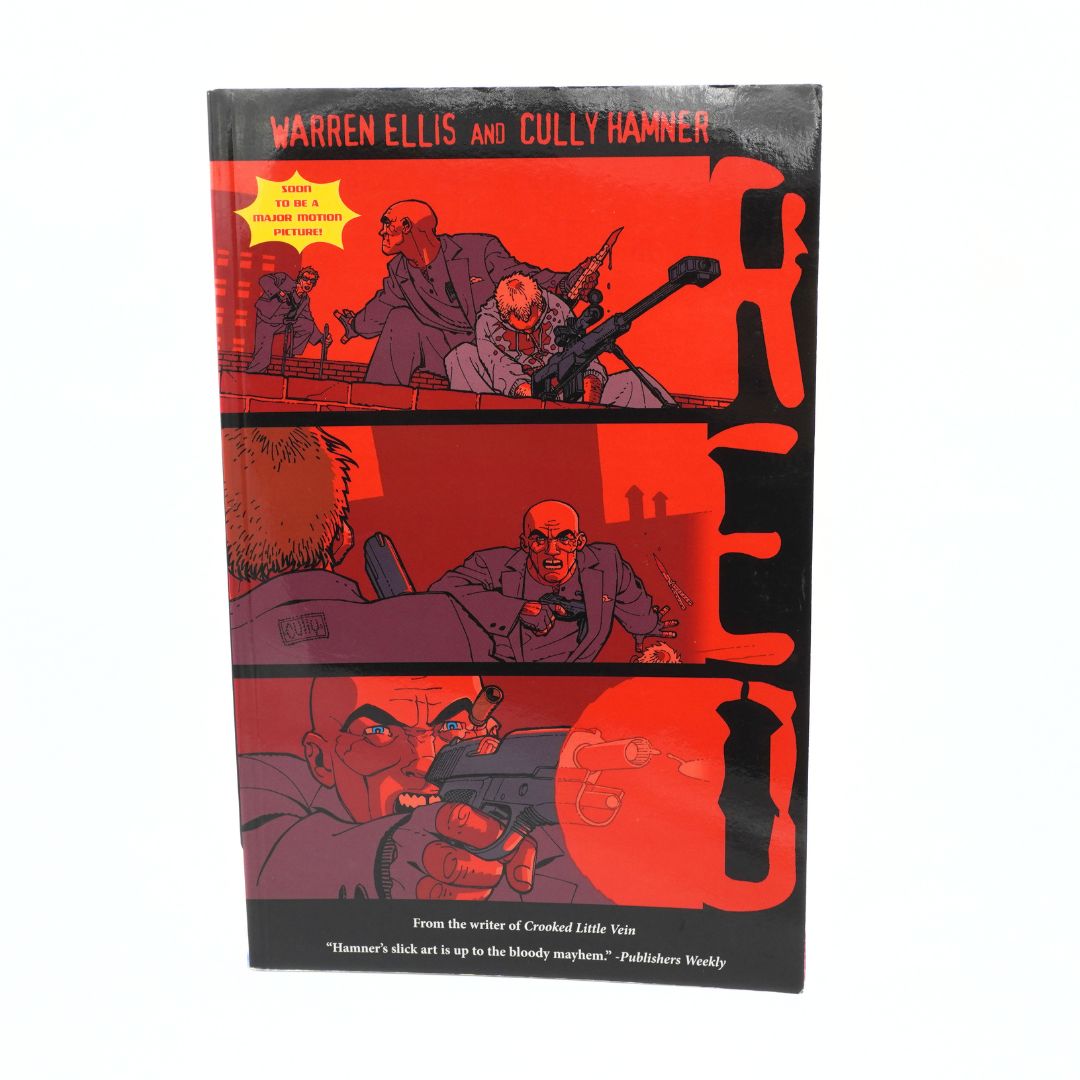 The book cover of 'Red' by Warren Ellis and Cully Hamner, featuring a bold red and black comic-style illustration with three horizontal panels and large vertical 'RED' lettering, photographed on a white background.