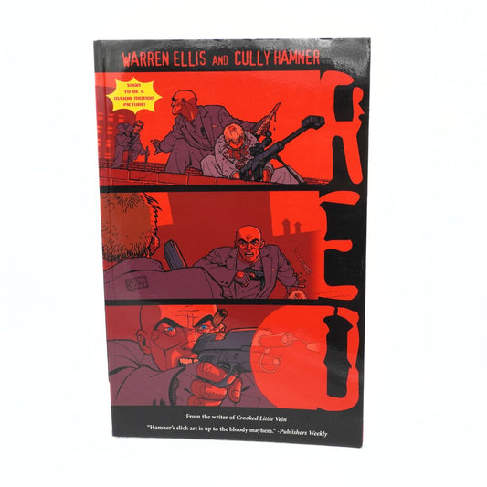 The book cover of 'Red' by Warren Ellis and Cully Hamner, featuring a bold red and black comic-style illustration with three horizontal panels and large vertical 'RED' lettering, photographed on a white background.