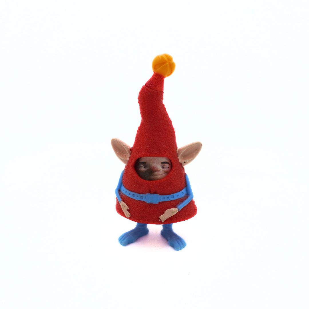 Small figurine of a creature with a red hat and blue outfit on a white background