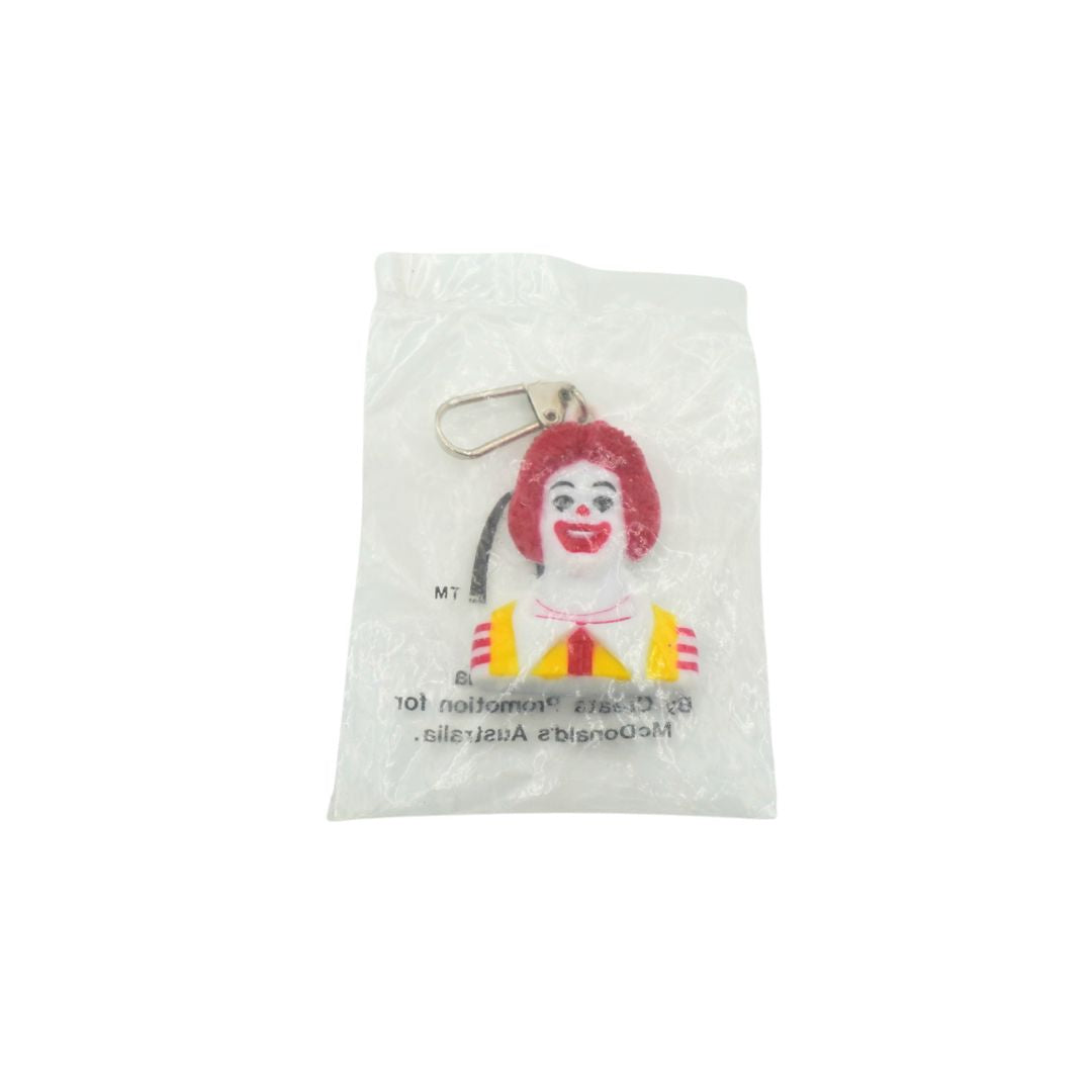 A Ronald McDonald keychain charm inside a clear plastic protective bag, featuring his signature red hair, yellow and red striped shirt, and white face paint, with a silver metal keyring attached.