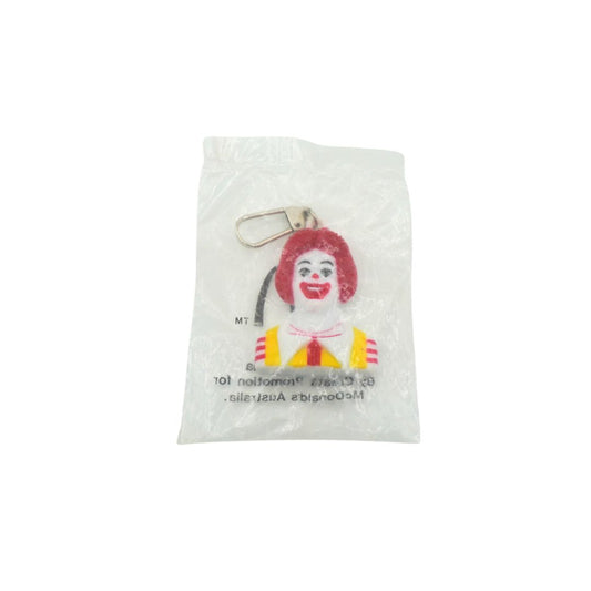 A Ronald McDonald keychain charm inside a clear plastic protective bag, featuring his signature red hair, yellow and red striped shirt, and white face paint, with a silver metal keyring attached.