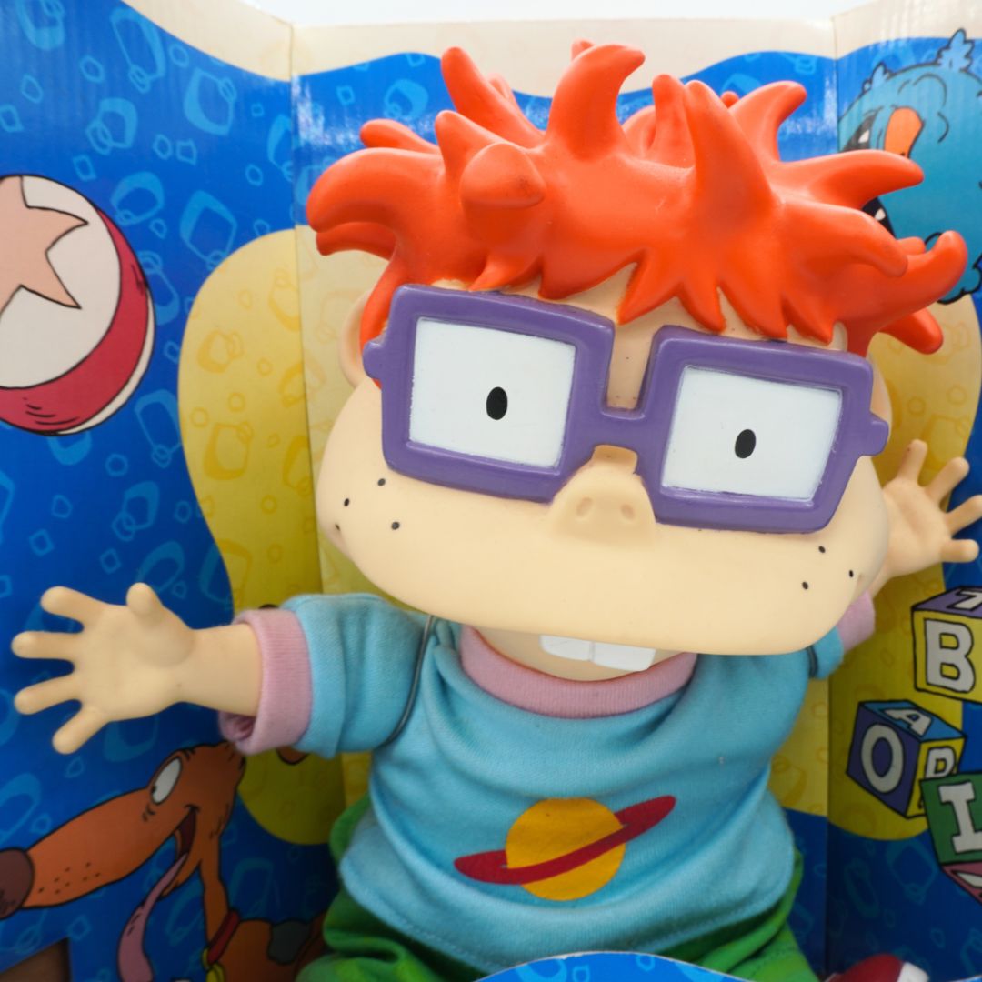Toy figure of a character with red hair and glasses in front of a colorful background